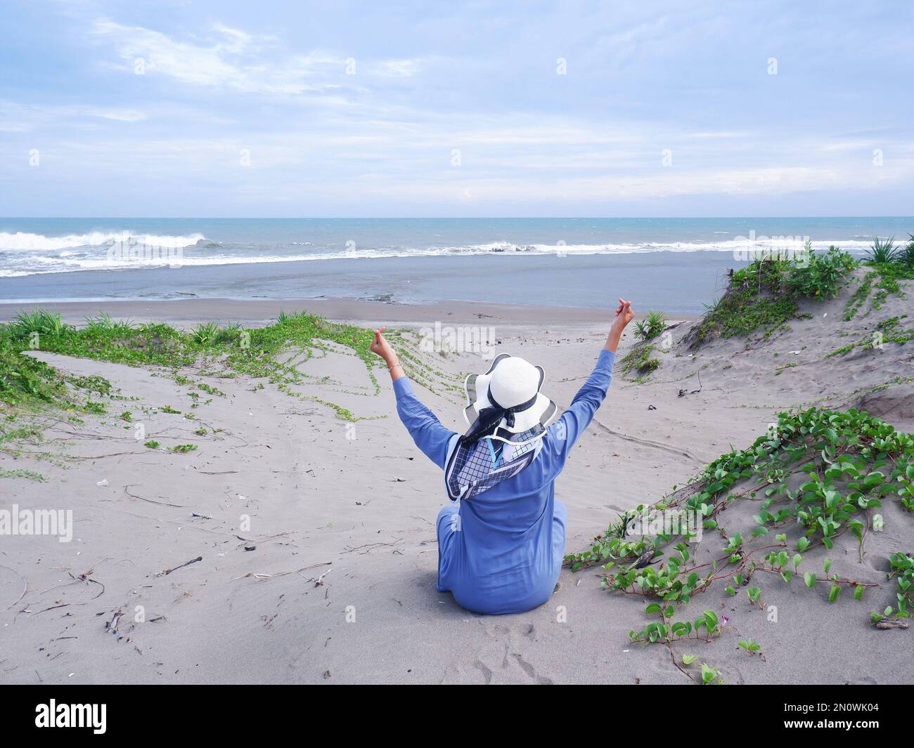 Der Rücken der Frau mit dem Hut am tropischen Strand, die auf dem Sandstrand saß und auf das Meer starrte, entstand dann Liebe aus der Hand. Rückgrat Stockfoto