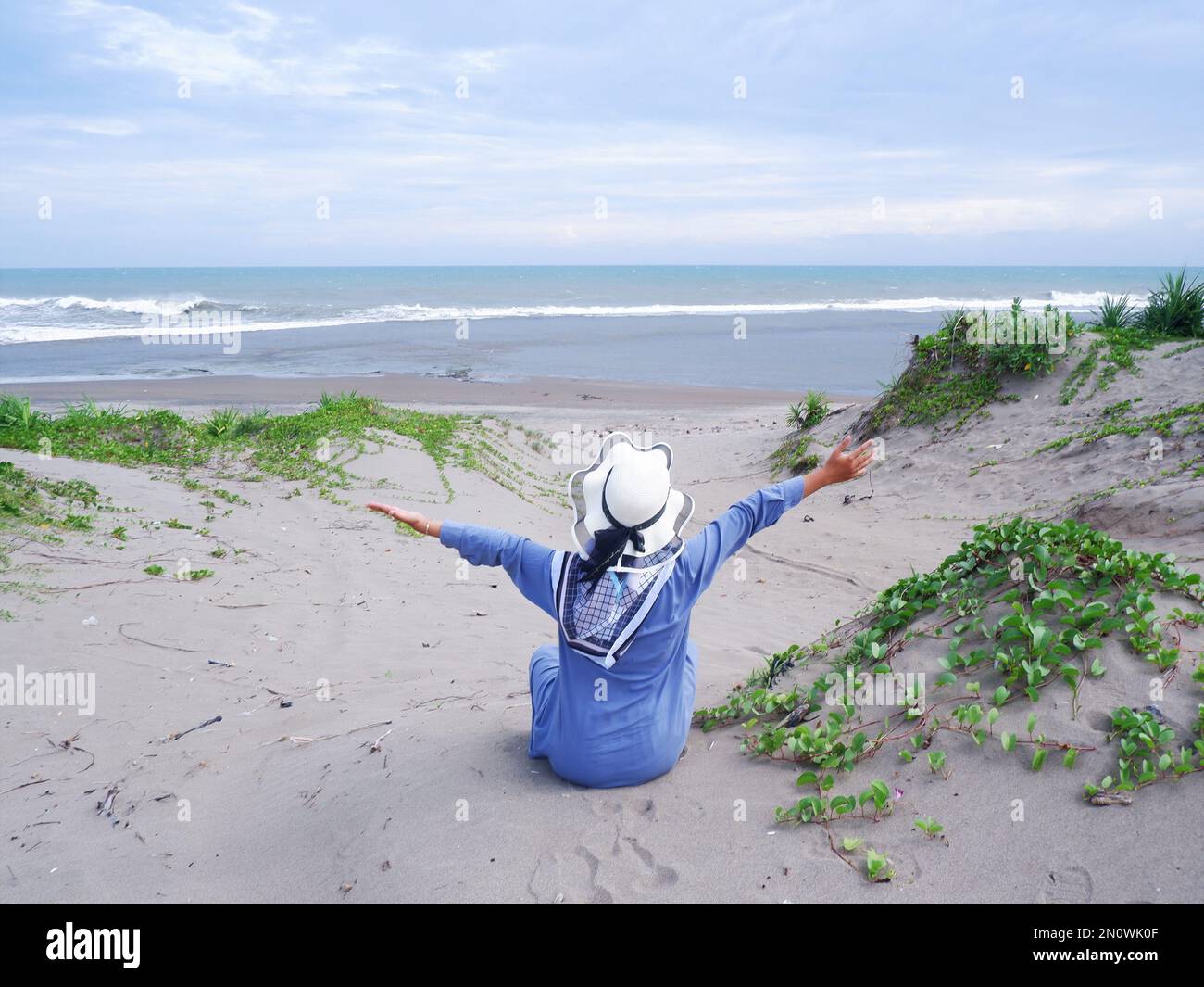 Der Rücken der Frau mit dem Hut am tropischen Strand, die auf dem Sandstrand saß und auf das Meer starrte, entstand dann Liebe aus der Hand. Rückgrat Stockfoto