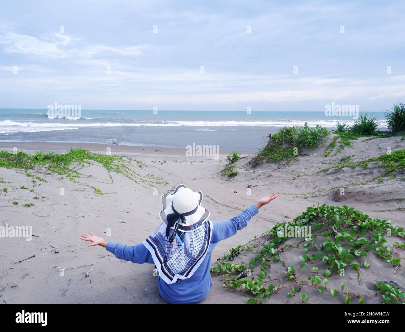 Die Frau mit dem Hut am tropischen Strand, die auf den Himmel und das Meer blickt Stockfoto