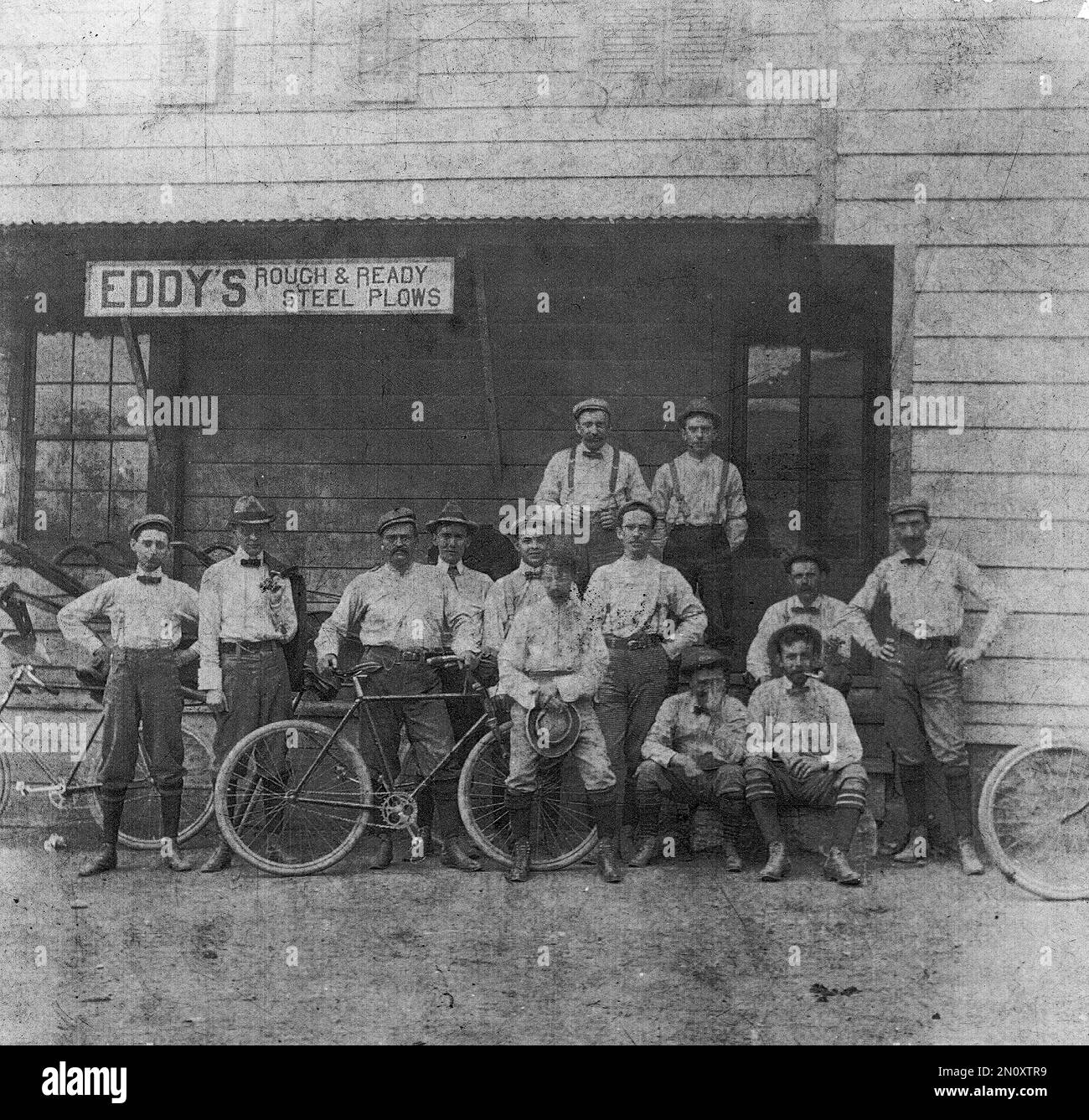 Old-Time Bicycles, Vintage Bikes, Men on Bikes um 1900, Jahrhundertwende, Eddy's Rough & Ready Steel Plows Storefront Stockfoto