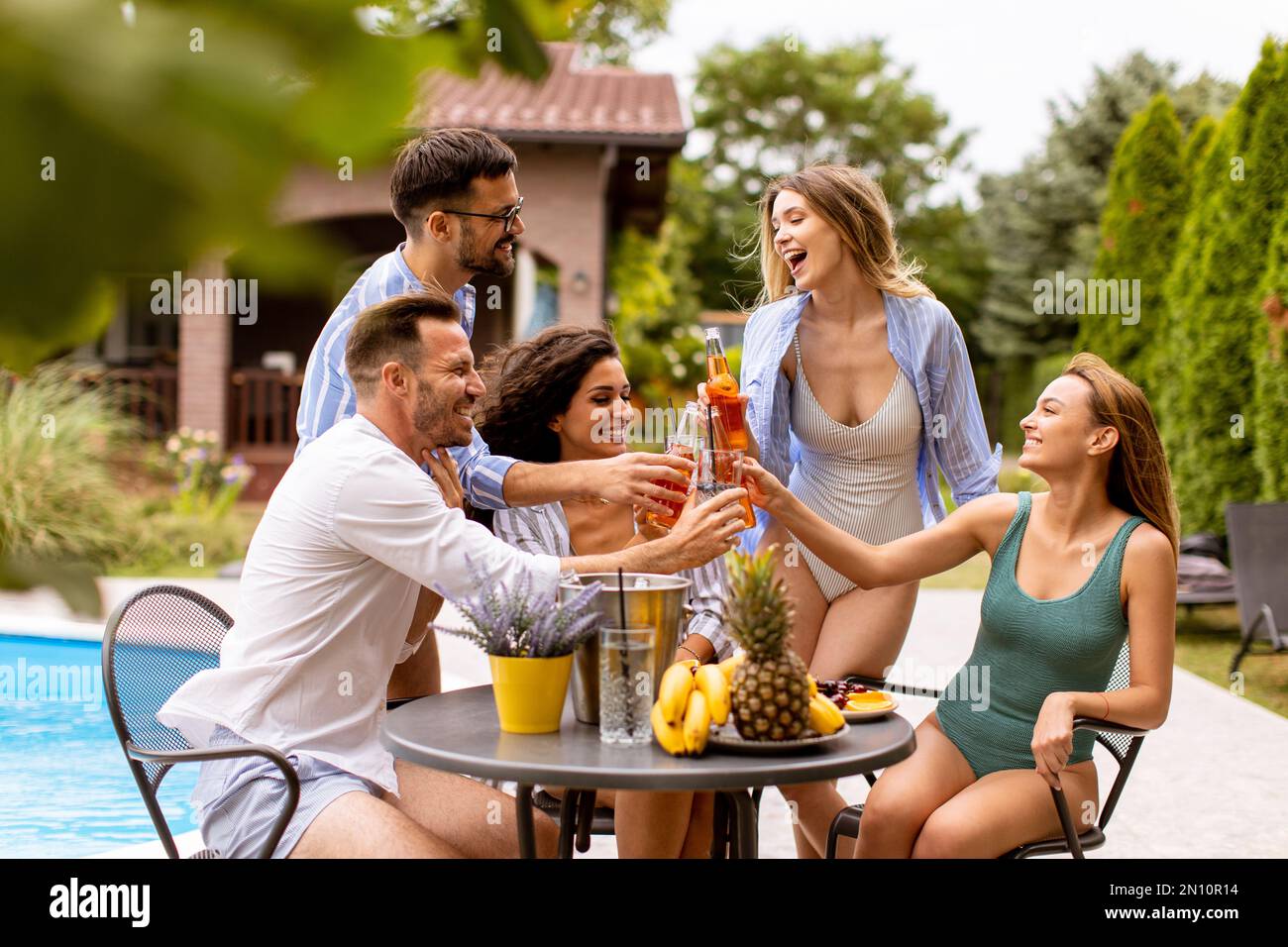 Eine Gruppe von glücklichen jungen Leuten, die mit Apfelwein am Pool im Garten jubeln Stockfoto