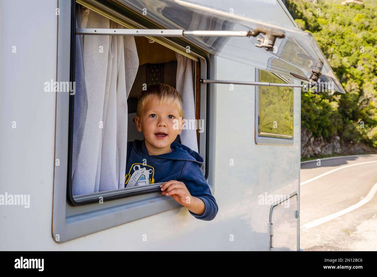Glücklicher kleiner Junge, der durch das Fenster des Wohnmobils schaute, das an der Straße geparkt war, Portugal, Europa Stockfoto