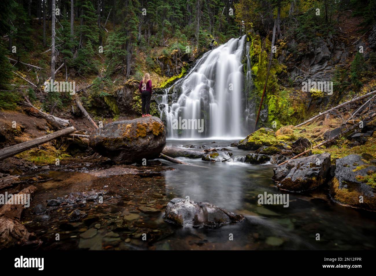 Junge Frau steht auf Stein, Wasserfall, Middle Tumalo Falls, lange Exposition, Tumalo Creek, Bend, Deschutes County, Oregon, USA, Nordamerika Stockfoto