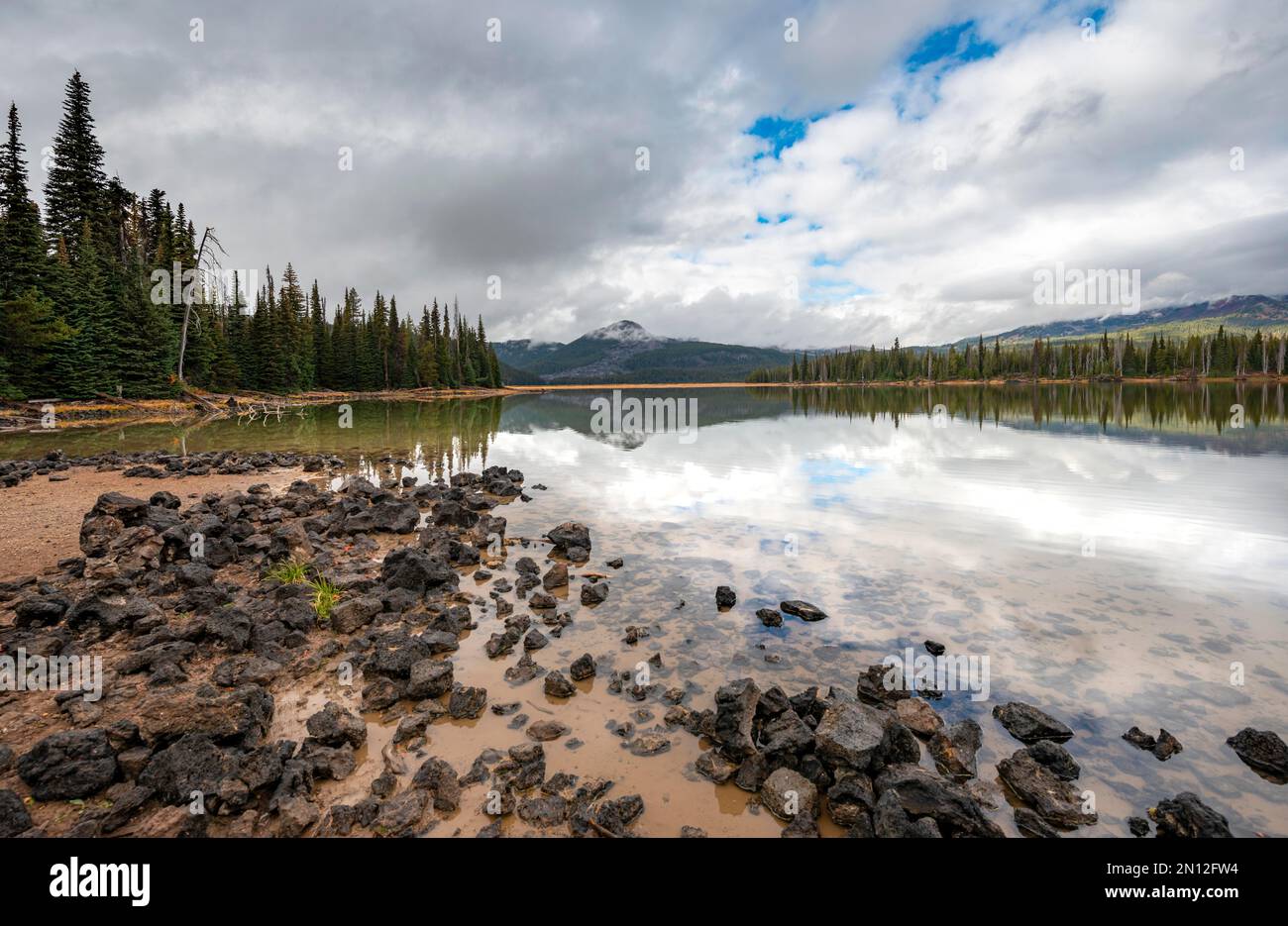 Schwarze Steine am Seeufer, eine Landschaft mit Wäldern im See, Sparks Lake, Oregon, USA, Nordamerika Stockfoto