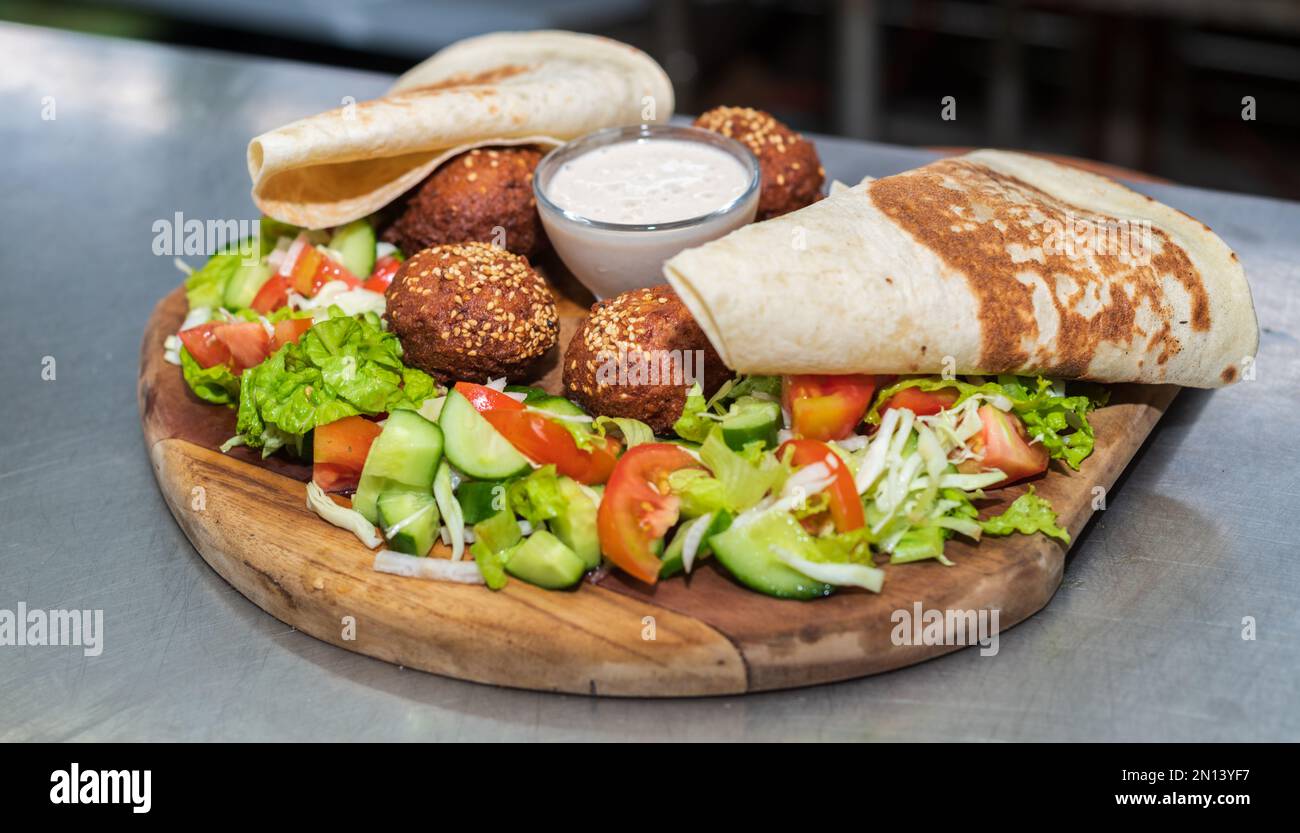 Köstliche Vorspeise Falafel auf einem Holzteller in der libanesischen Restaurantküche. Fladenbrot, Gemüsesalat und Tahini-Sauce. Stockfoto