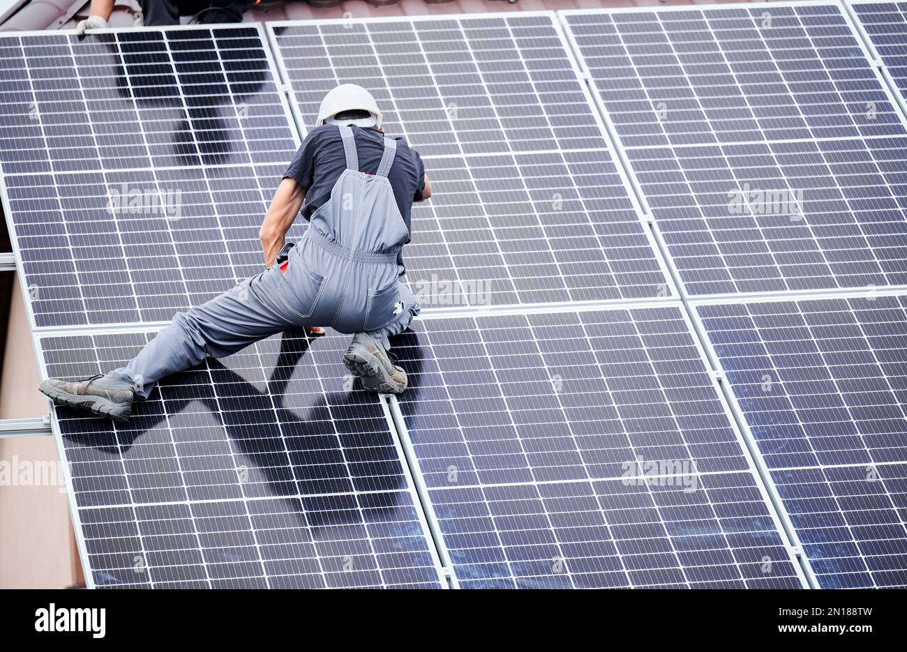 Männer Techniker montieren Photovoltaik-Solarmodule auf dem Dach des Hauses. Rückansicht des Helmbauers zur Installation eines Solarmoduls im Außenbereich. Konzept alternativer und erneuerbarer Energien. Stockfoto
