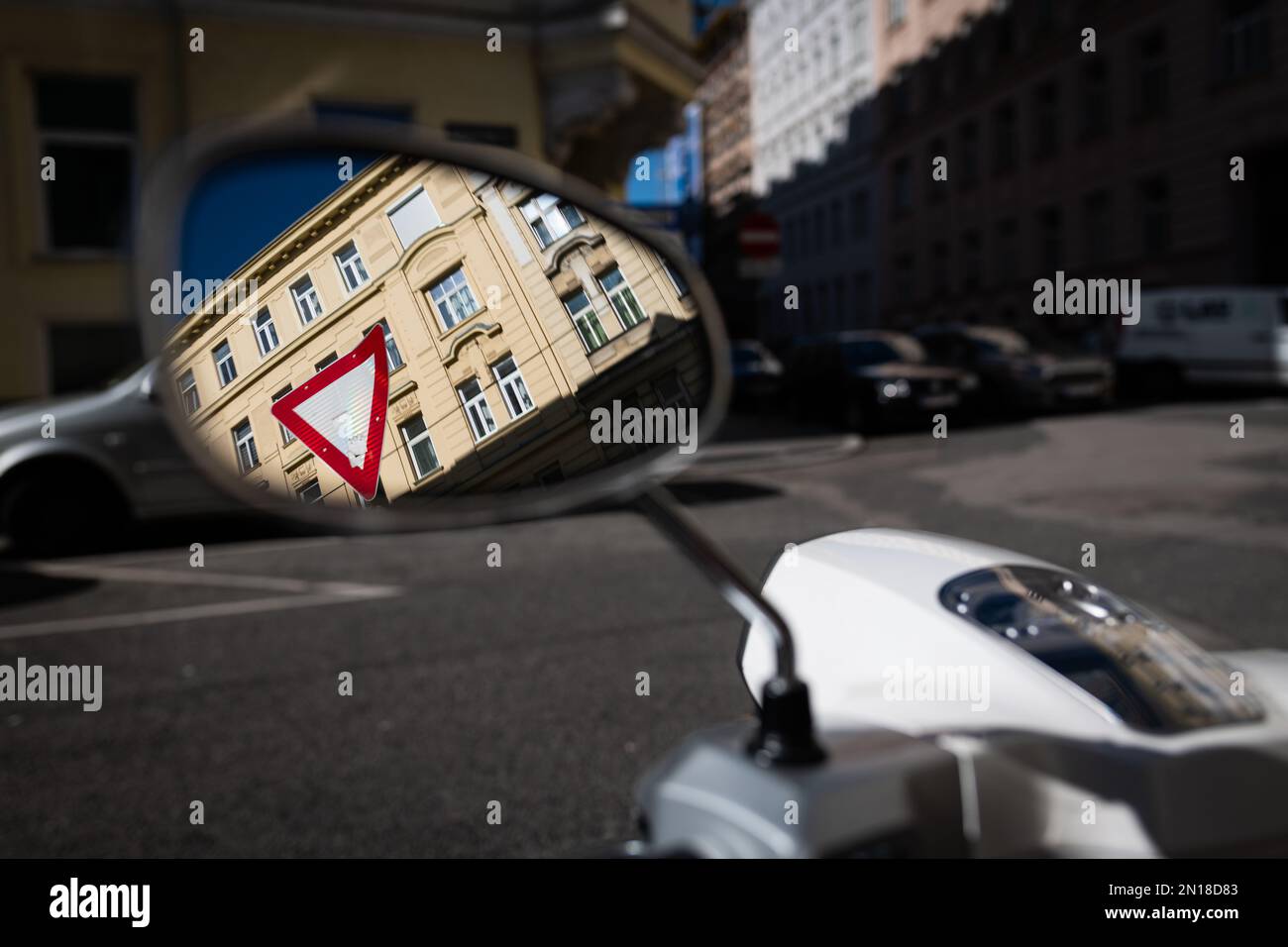 Reflexion eines Verkehrsschilds vor einem Gebäude im Seitenspiegel eines Motorrads, das auf einem Parkplatz in einer wiener Straße steht Stockfoto