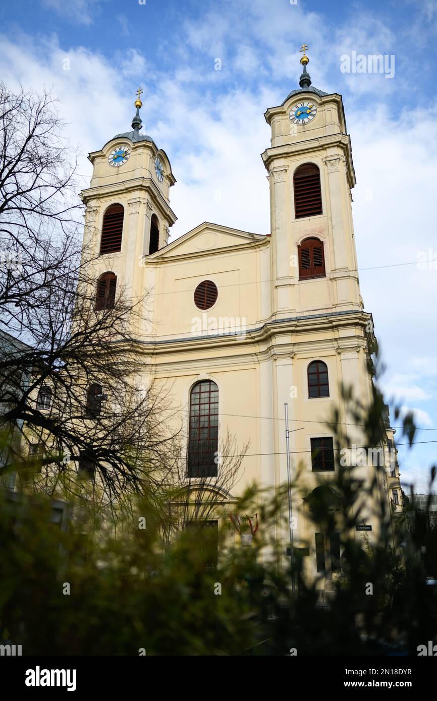 Einfache alte gelbe katholische Kirche mit zwei identischen Uhrentürmen in Lichtental, Wien, Österreich Stockfoto