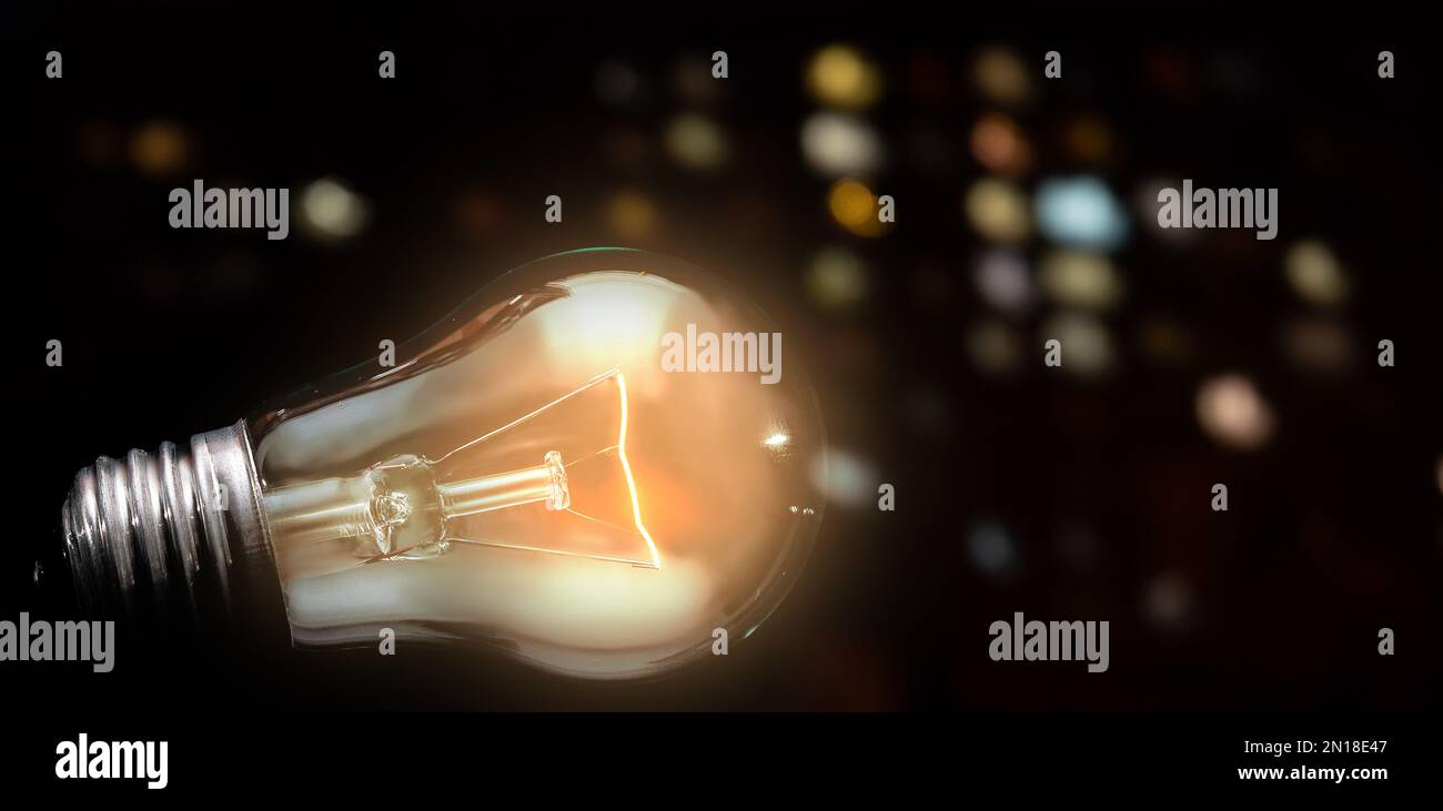 Nahaufnahme der Wolfram-Glühbirne mit Licht auf dunklem Hintergrund und Nachtlicht der Stadt Stockfoto