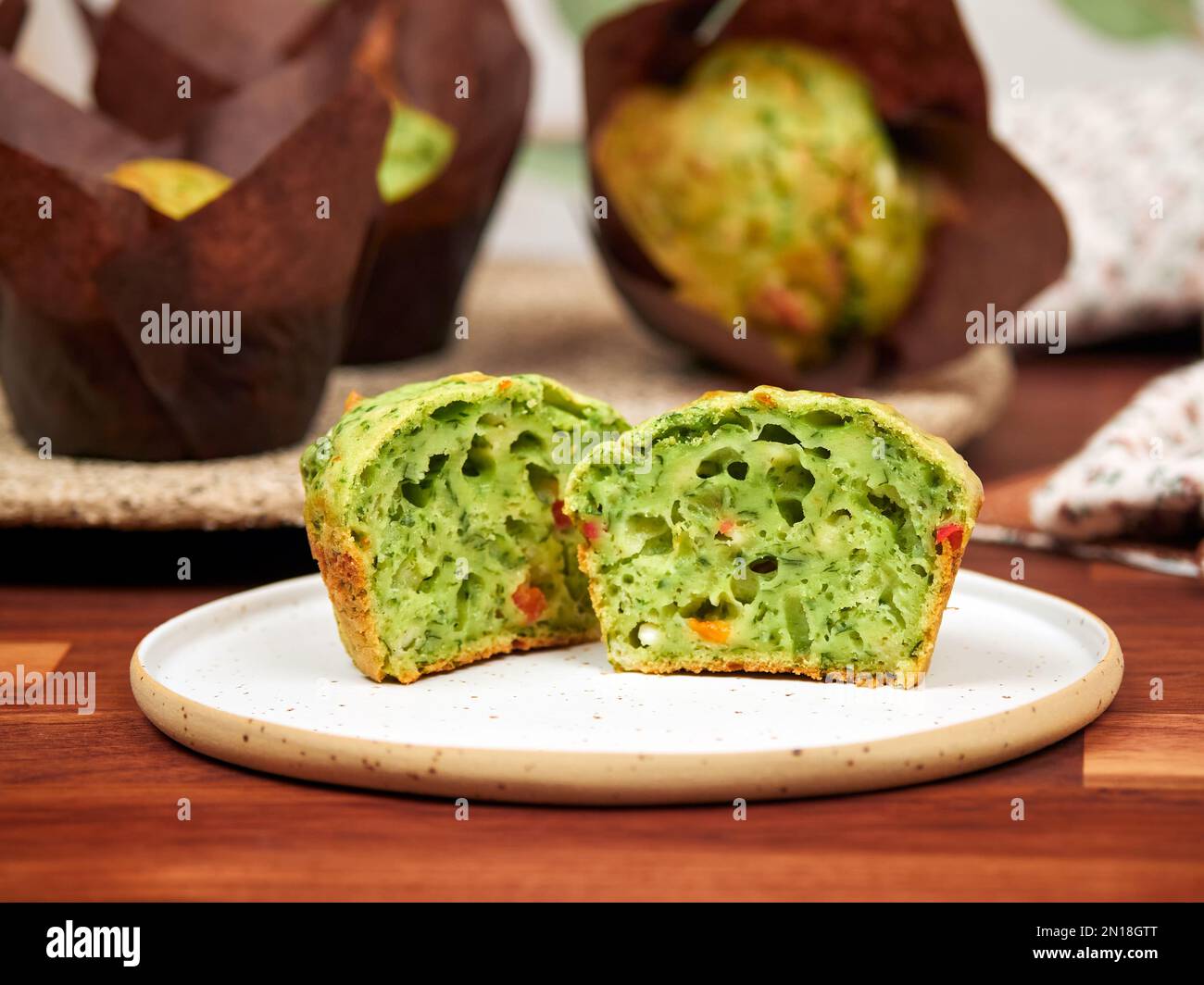 Hausgemachte herzhafte Muffins mit Spinat, rotem Glockenpapier und Feta, in braunen Papiermuffin-Trägern, auf einer Keramikplatte Stockfoto