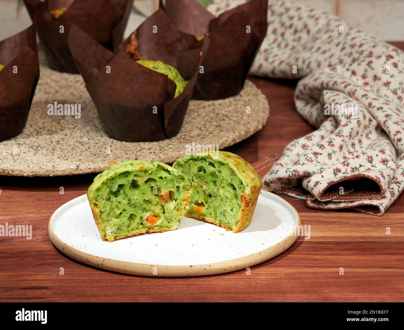 Hausgemachte herzhafte Muffins mit Spinat, rotem Glockenpapier und Feta, in braunen Papiermuffin-Trägern, auf einer Keramikplatte Stockfoto