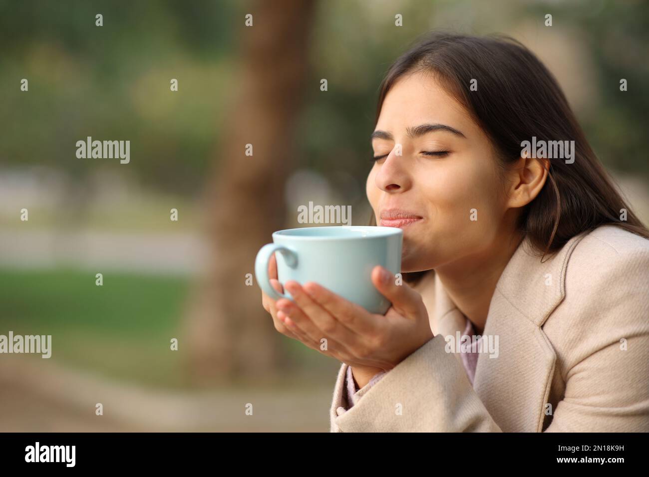 Eine Frau bei Sonnenuntergang im Winter, die Kaffee in einem Park riecht Stockfoto