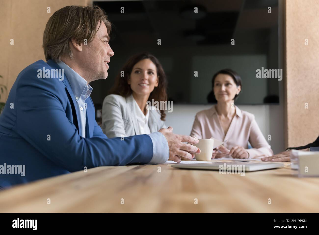 Positiver, engagierter, reifer Geschäftsmann, der an einem Tisch in einer Teambesprechung sitzt Stockfoto
