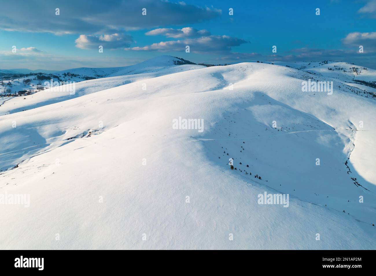Luftaufnahme der schneebedeckten Bergspitze, die von der untergehenden Sonne bei Sonnenuntergang in Zlatibor, Serbien, von Drohne pov beleuchtet wird. Stockfoto