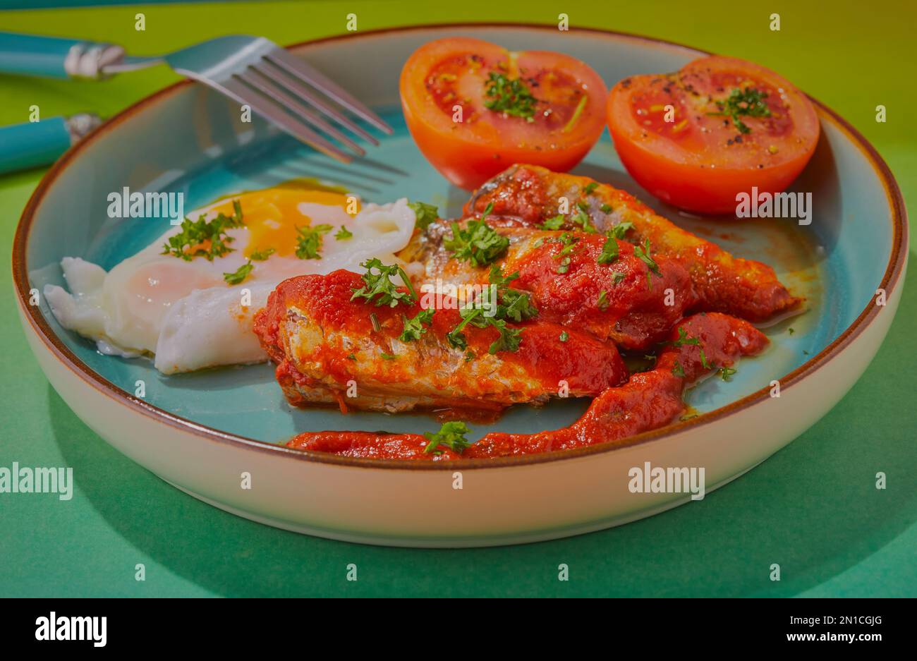 Sardinen in Tomatensoße mit pochierten Eiern und Tomaten. Stockfoto
