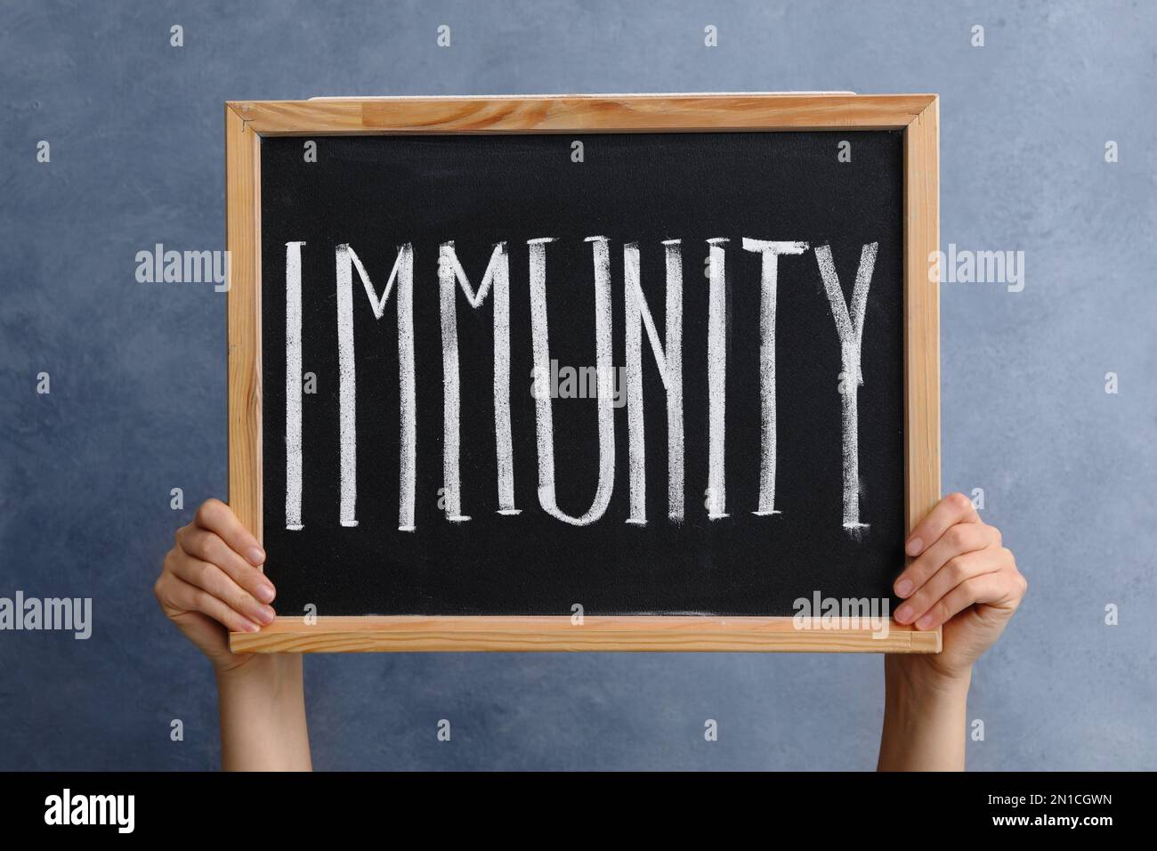 Eine Frau, die eine kleine Tafel hält, mit dem Wort "Immunität" auf blauem Hintergrund, Nahaufnahme Stockfoto