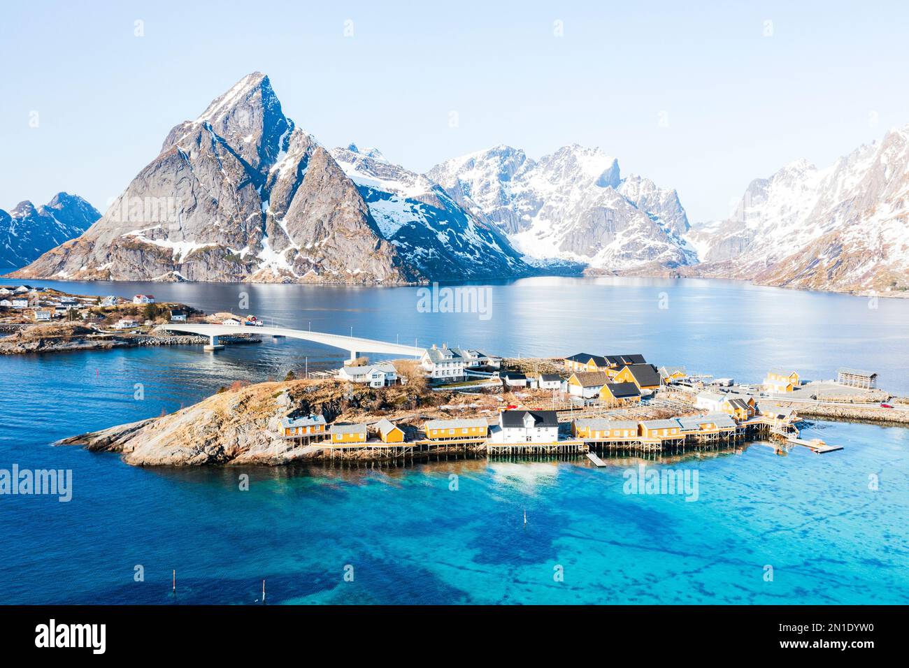 Blick aus der Vogelperspektive auf den Berggipfel Olstind und das türkisfarbene Meer rund um das Dorf Sakrisoy und die reine Bucht, die Lofoten-Inseln, Norwegen, Skandinavien und Europa Stockfoto