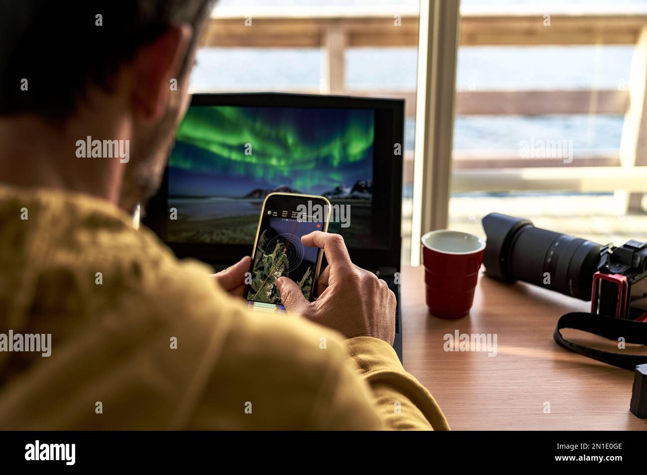 Ein Mann, der auf einem Smartphone Karten ansieht, während er mit einem Laptop, den Lofoten-Inseln, Norwegen, Skandinavien und Europa arbeitet Stockfoto