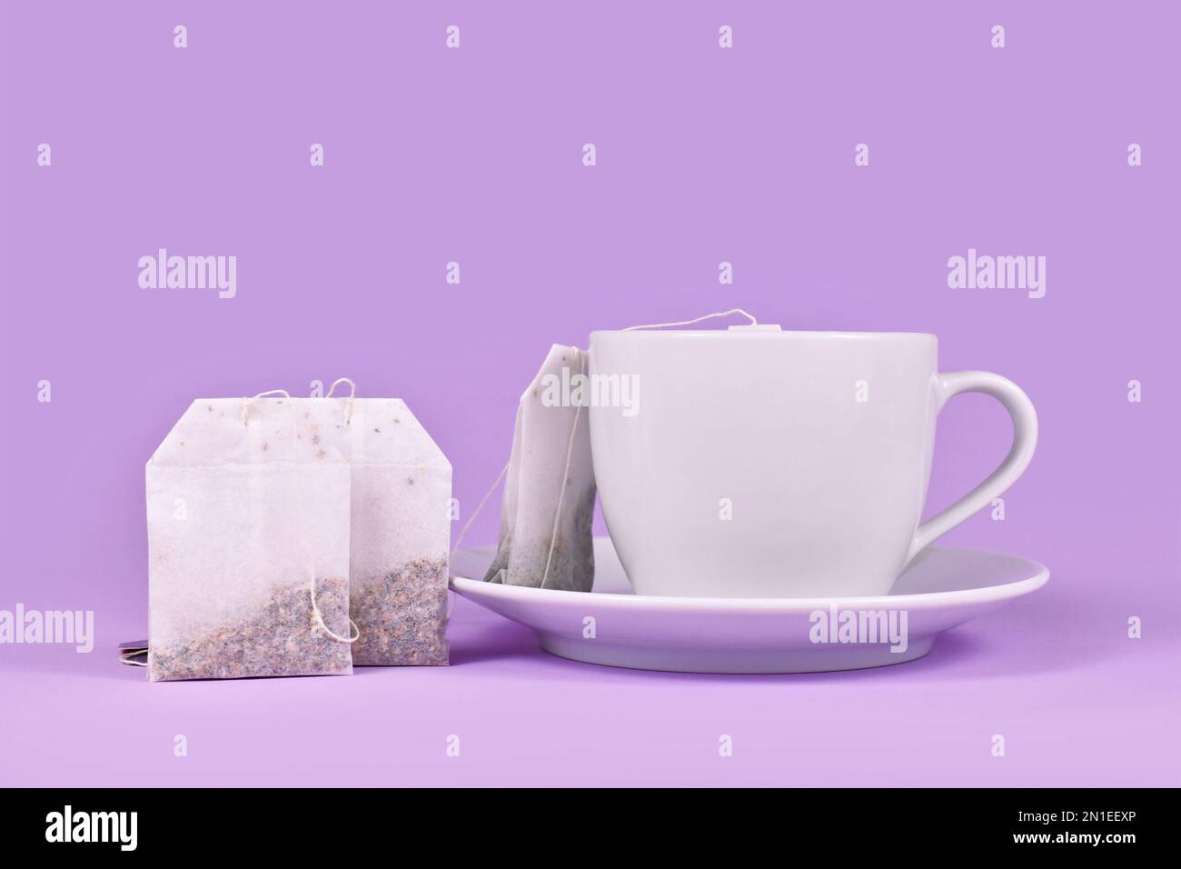 Teetasse mit Kräuterteebeuteln auf violettem Hintergrund Stockfoto
