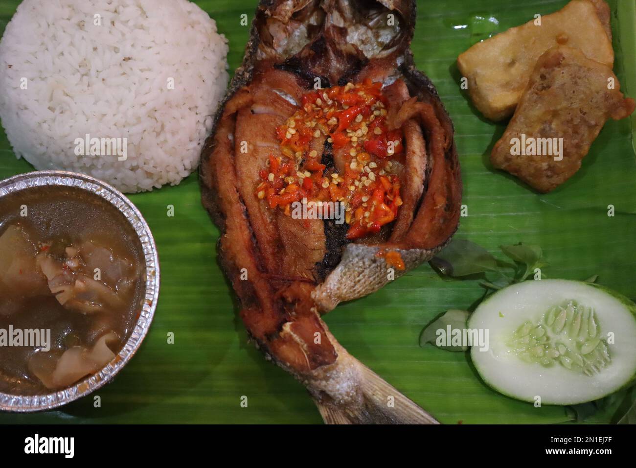 Gebratener Fisch mit Sambal, Gemüse aus Indonesien mit weißem Reis, isoliert auf Bananenblatt Stockfoto