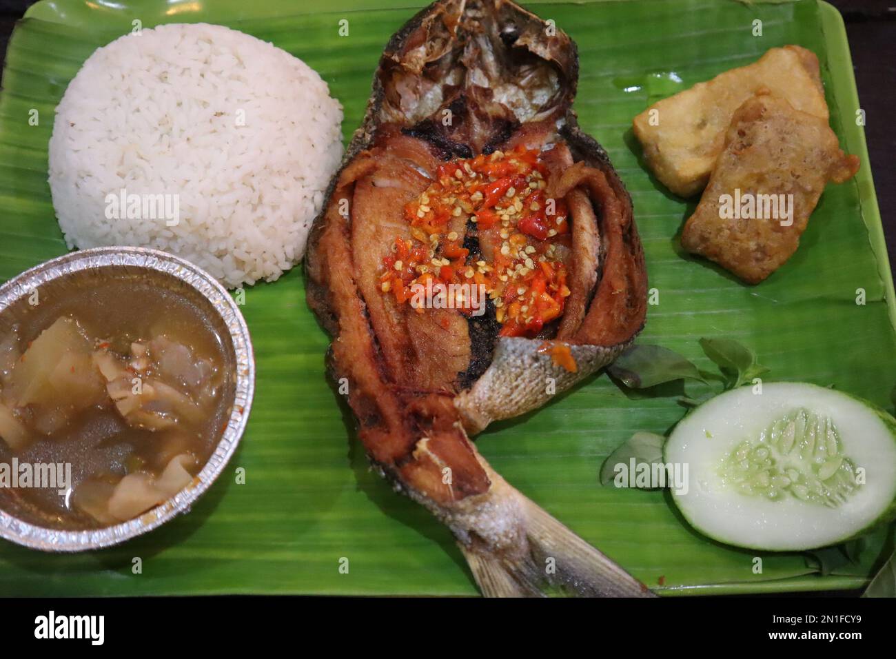 Gebratener Fisch mit Sambal, Gemüse aus Indonesien mit weißem Reis, isoliert auf Bananenblatt Stockfoto
