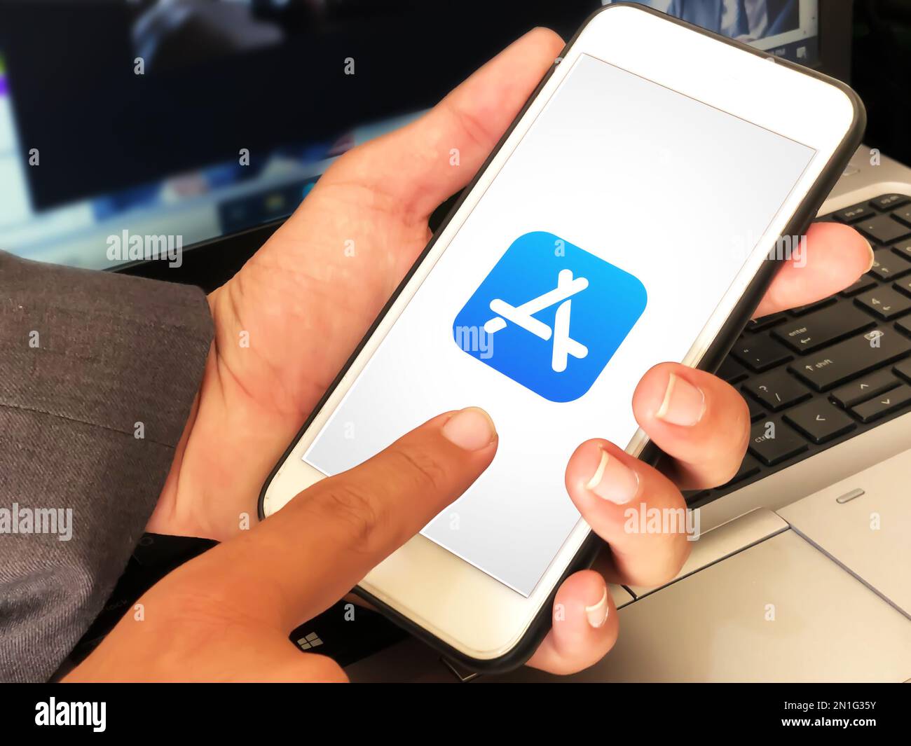 Mann, der den Apple Store auf dem iPhone benutzt, indem er den Bildschirm und den Laptop im Hintergrund berührt, Leitartikel Stockfoto