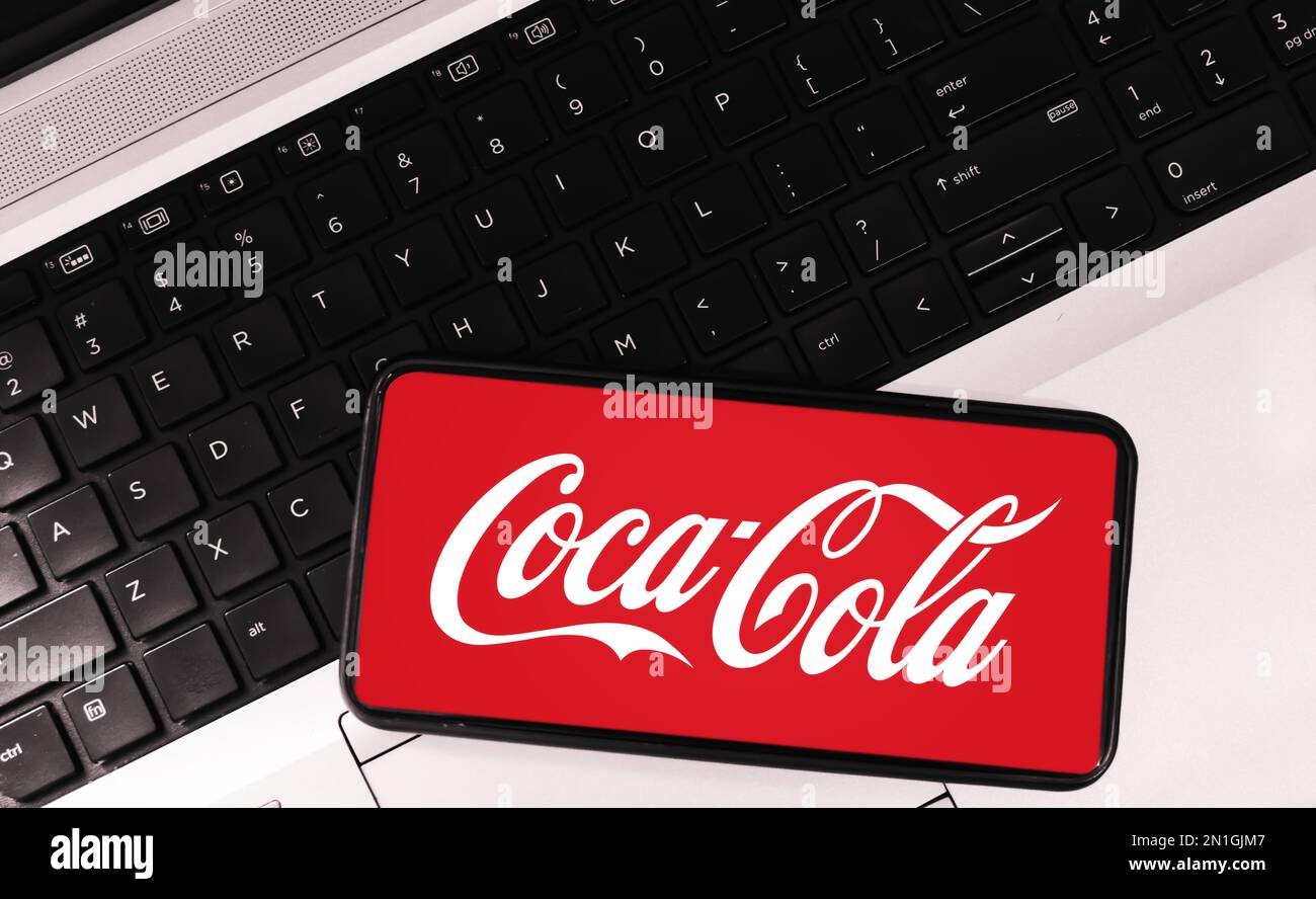 Coca Cola mit Softdrink auf dem Mobilbildschirm mit Laptop im Hintergrund, redaktionelles Konzept Stockfoto