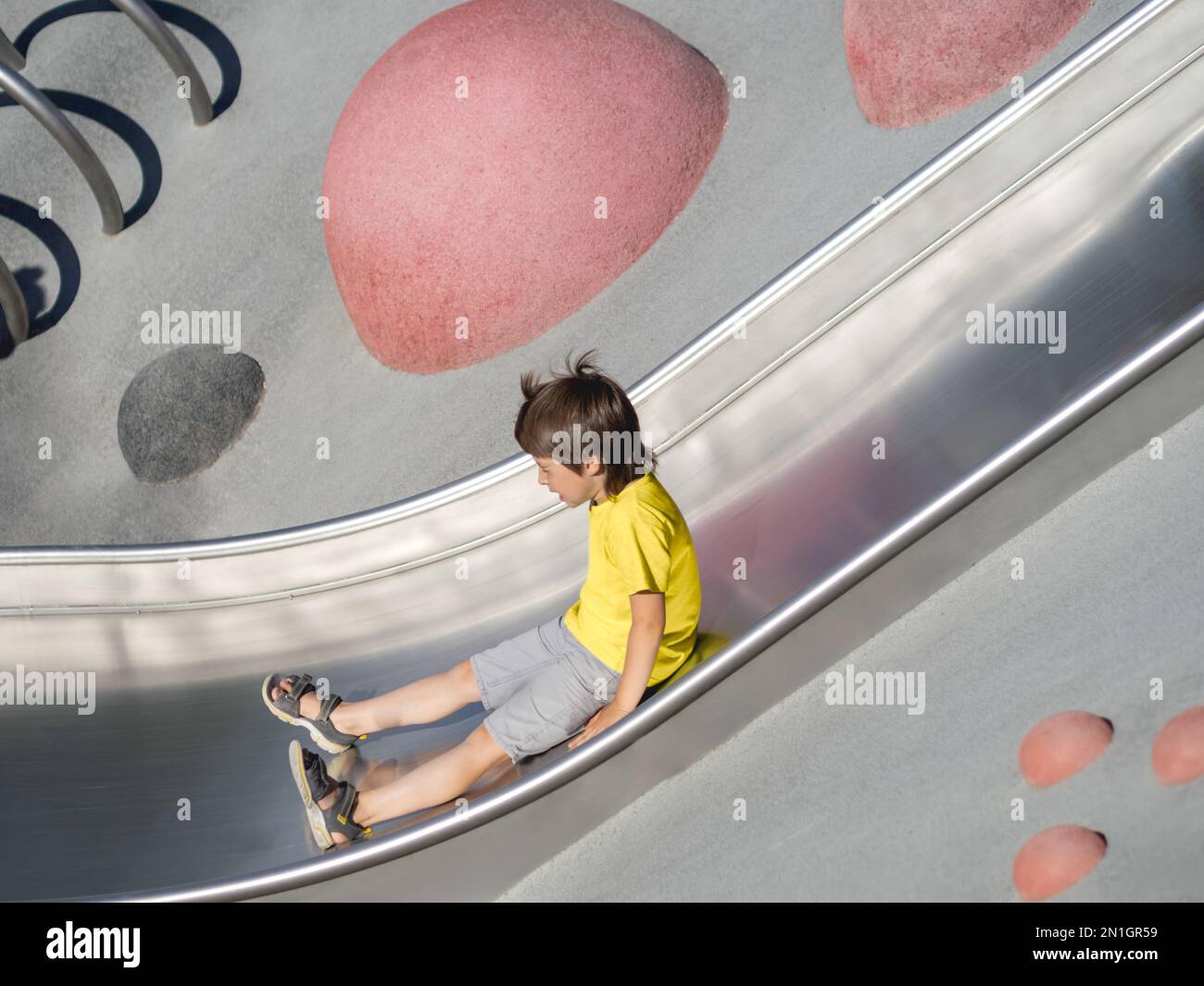 Ein Junge mit geschlossenen Augen fährt auf einer Metallrutsche auf einem modernen Kindersport- und Spielplatz. Das Kind überwindet die Angst und lernt neue Dinge. Aktive Freizeit Stockfoto