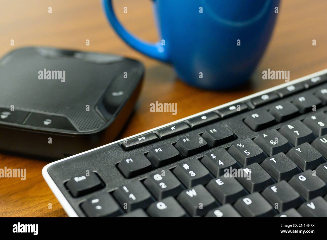 Vergrößerung der Computertastatur mit Lautsprecher für Telefon, Konferenzgespräche und eine Tasse Kaffee auf dem Holzschreibtisch, um den Tag festzuhalten Stockfoto