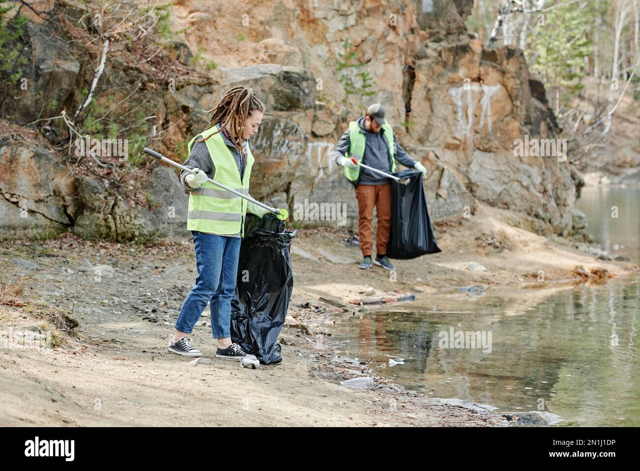 Junge Leute säubern das Seeufer, verwenden Spezialwerkzeuge zum Aufsammeln von Müll Stockfoto