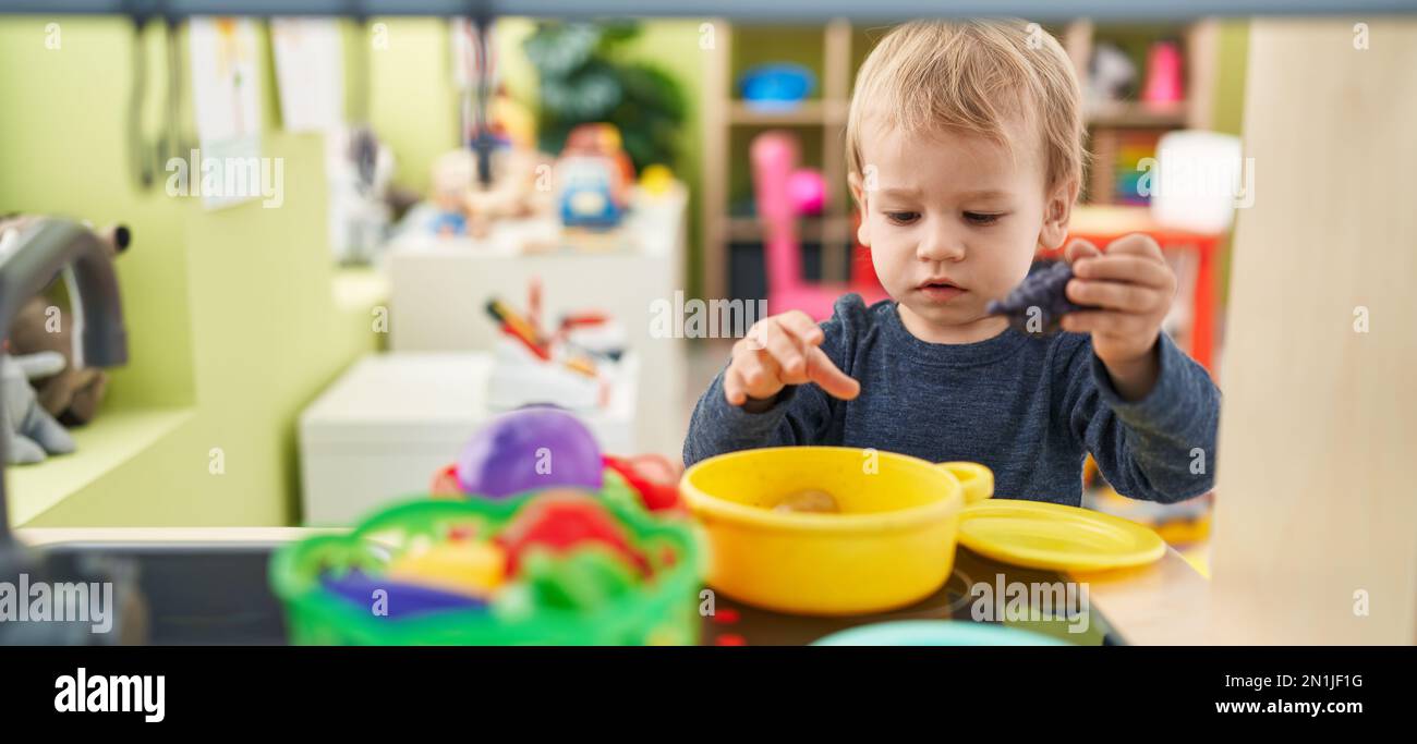 Ein bezauberndes blondes Kleinkind, das im Kindergarten mit der Spielküche spielt Stockfoto