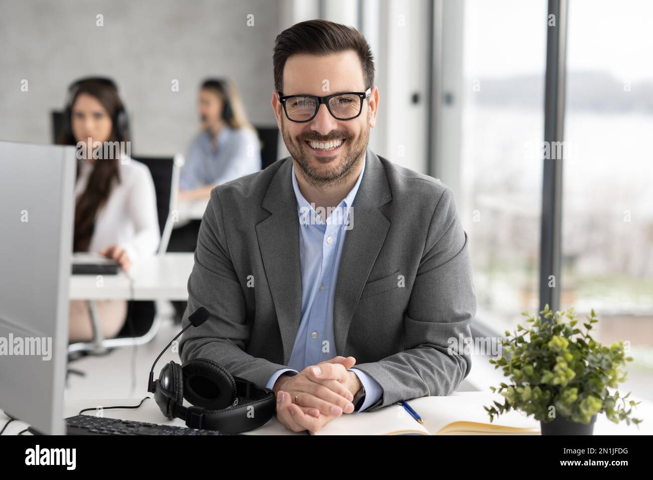 Lächelnder, bärtiger Geschäftsmann mit Brille im Callcenter-Büro Stockfoto