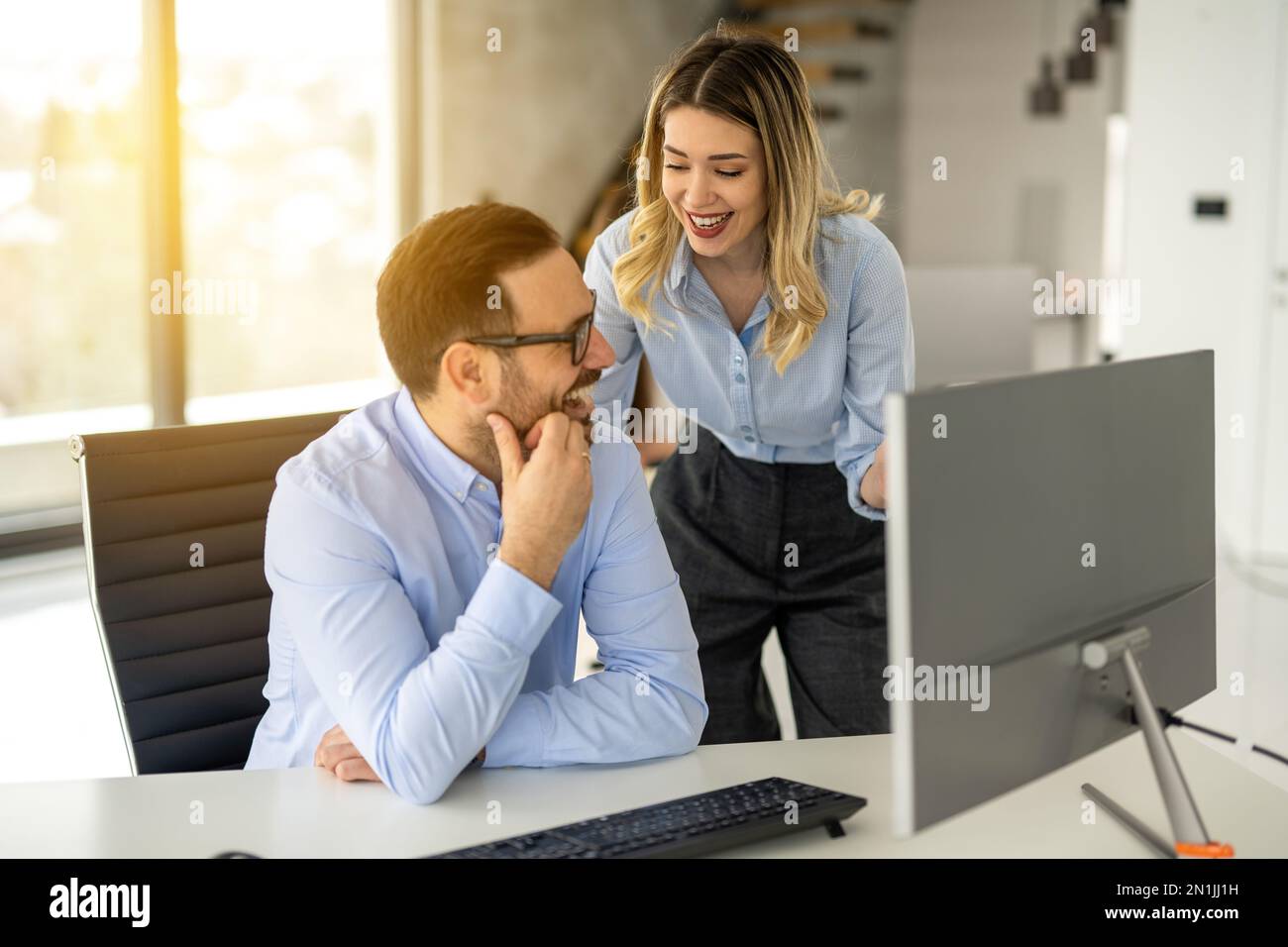 Fröhliche Geschäftsfrau und Mann, die sich während eines Meetings vor dem Computer in einem modernen Büro unterhalten. Stockfoto