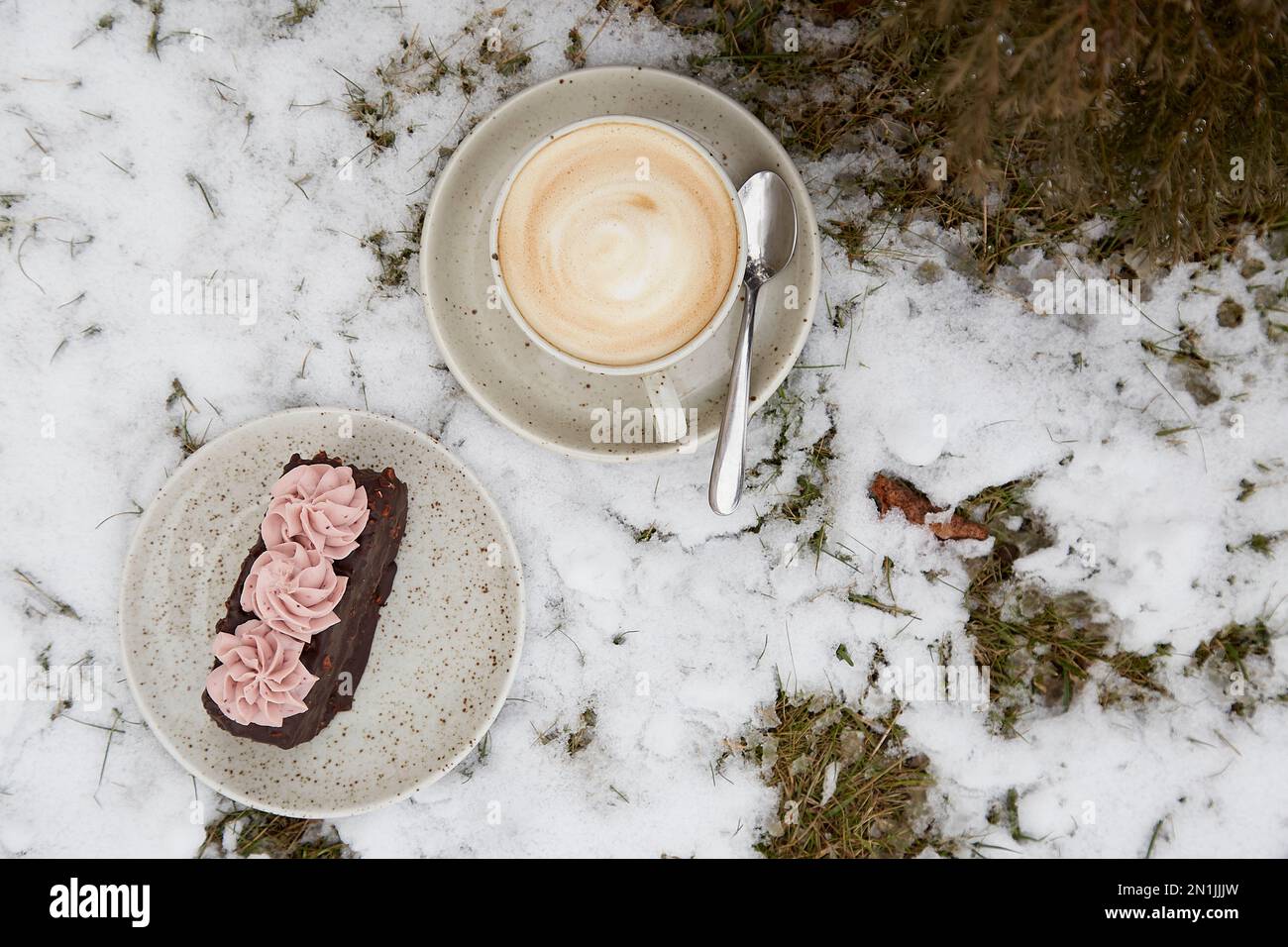 Vegane Brownie-Kuchen-Dessert mit einer Tasse Cappuccino im Freien an verschneiten Tagen. Kaffee mit Dessert. Winterästhetik. Stockfoto
