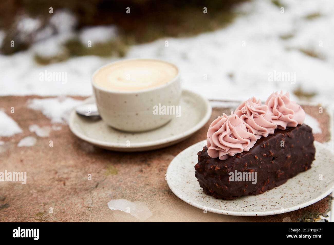 Veganer Brownie-Kuchen mit einer Tasse Cappuccino draußen. Kaffee mit Dessert. Winterästhetik. Stockfoto