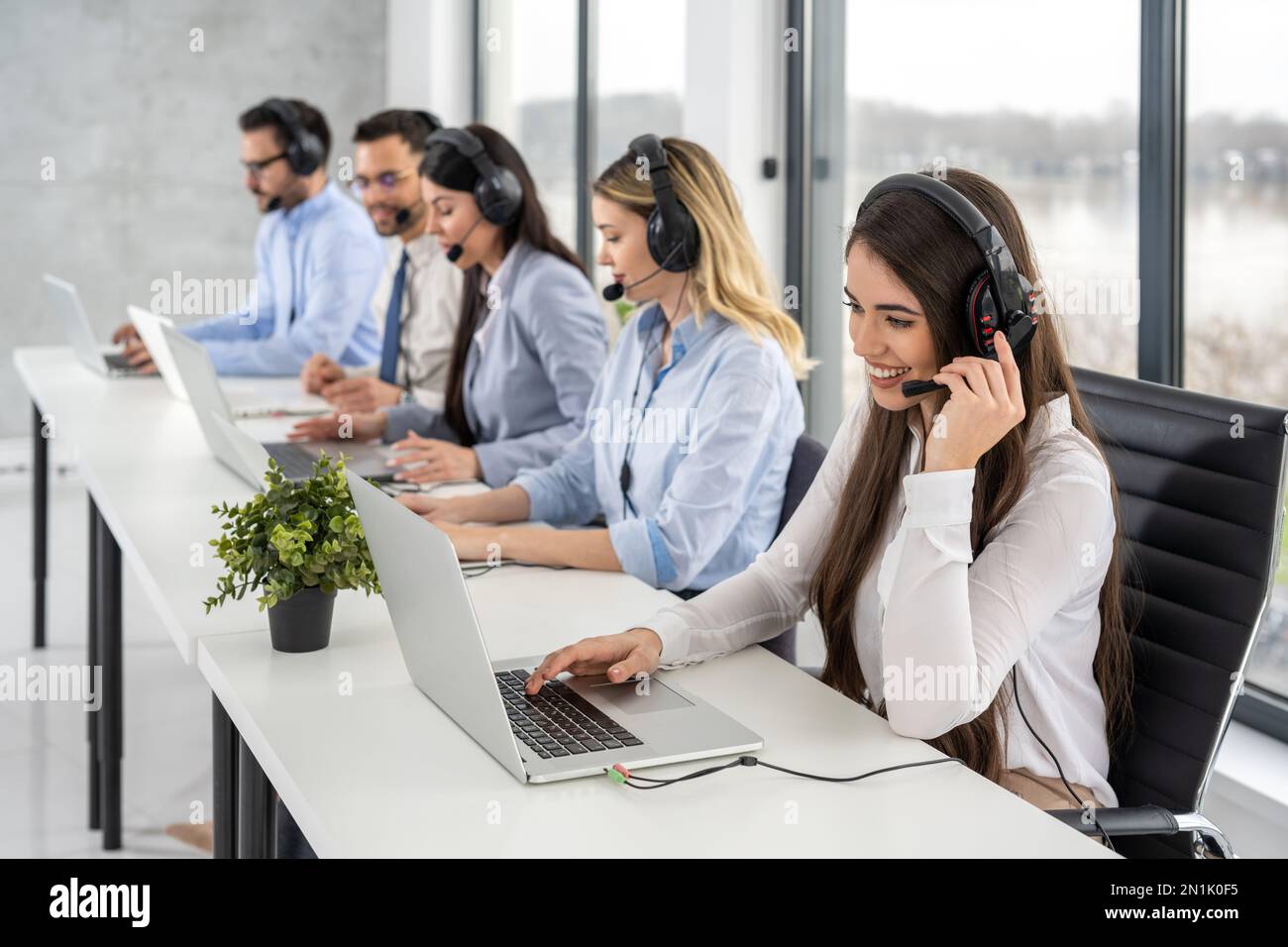 Gruppe von freundlichen, professionellen Kundendienstmitarbeitern, die mit Kunden interagieren, während sie Online-Chats im Callcenter-Büro führen. Stockfoto