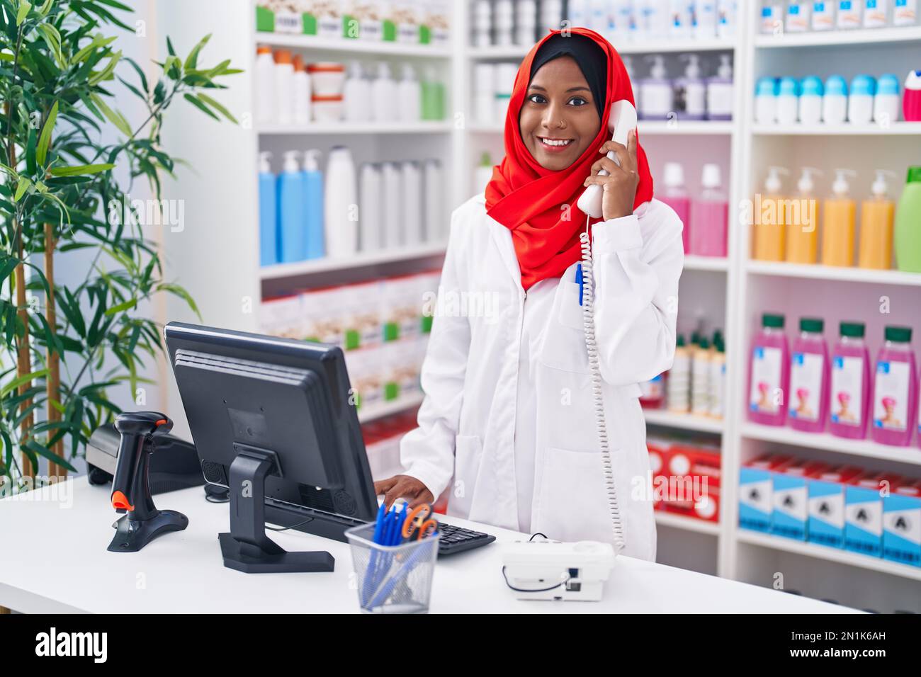 Eine junge, schöne Apothekerin, die telefoniert, indem sie einen Computer in der Apotheke benutzt Stockfoto