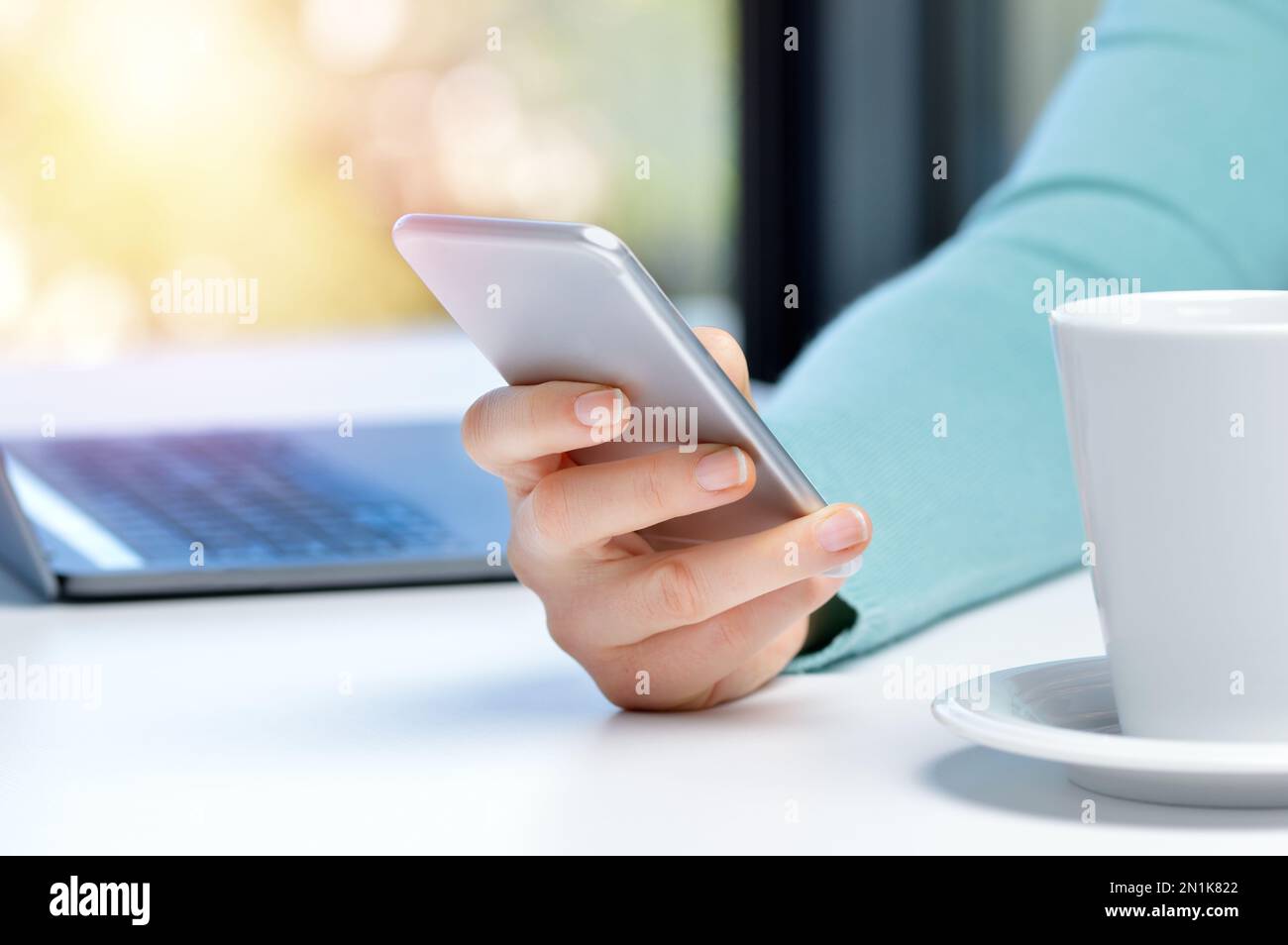 Freigestellte Aufnahme einer Geschäftsfrau, die ein Mobiltelefon und einen Laptop an seinem Schreibtisch benutzt Stockfoto