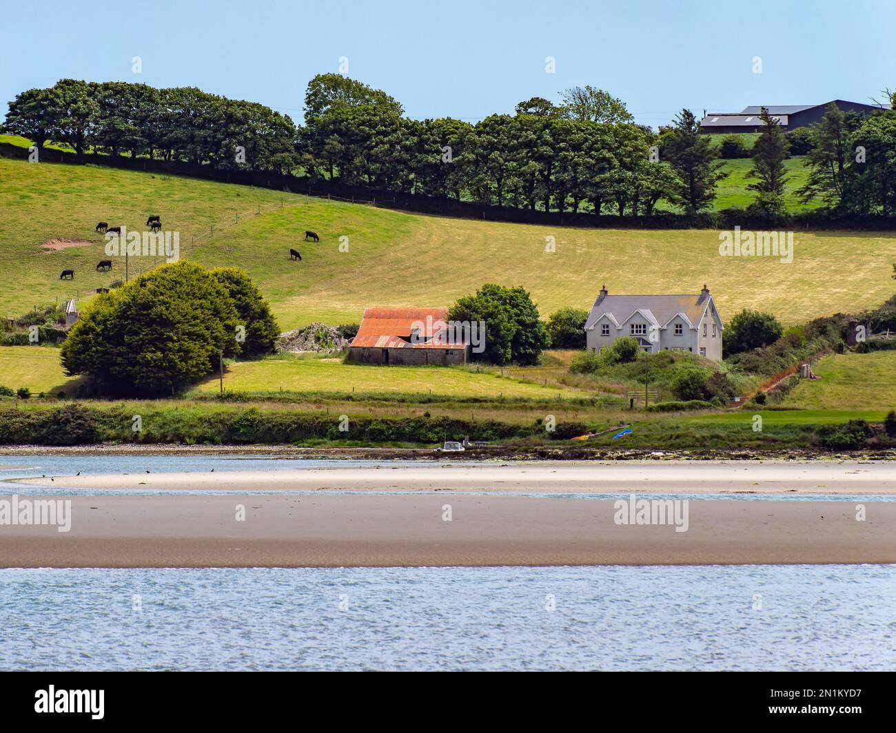 Ein Haus am grünen, hügeligen Ufer der Clonakilty Bay. Ländliche irische Landschaft. Die malerische Natur Irlands im Sommer, Haus in der Nähe von grünen Bäumen und bsb Stockfoto