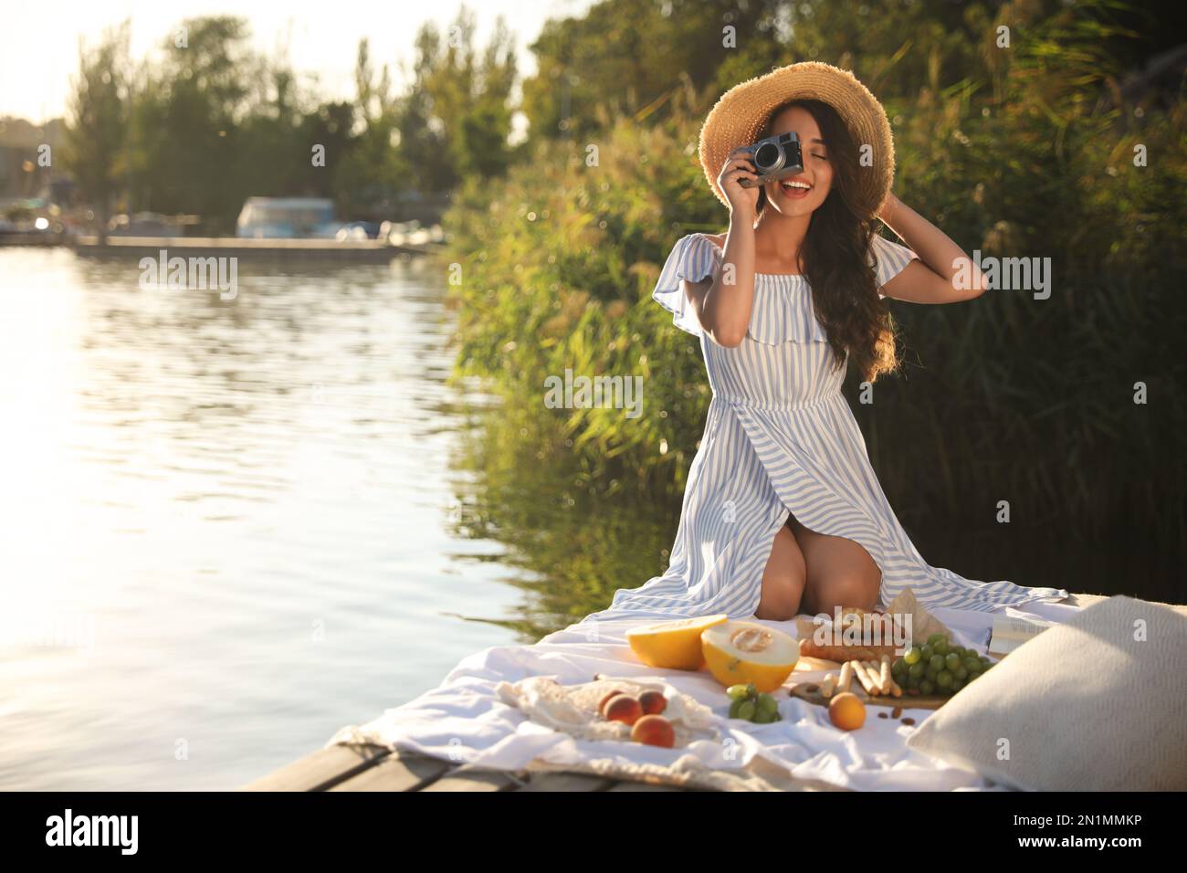 Junge Frau mit Kamera am Pier beim Picknick Stockfoto