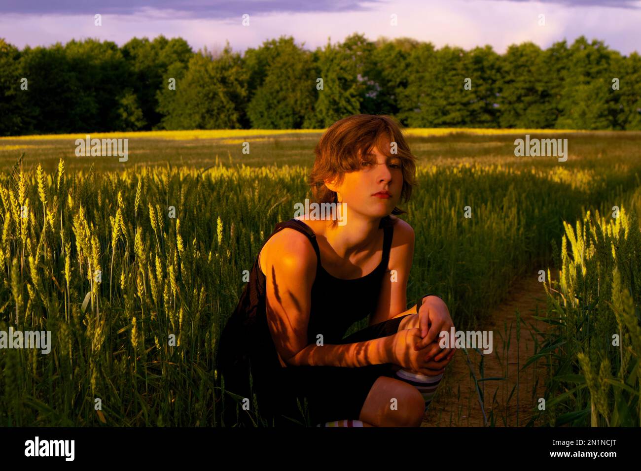 Ein Teenager sitzt auf dem Feld inmitten reifer Körner, die ein blumiges, tätowierähnliches Muster auf ihren Arm werfen. Stockfoto