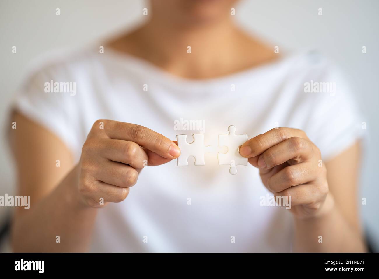 Nahaufnahme der Hand einer Frau, die zwei Puzzles aus weißem Papier zusammenhält. Verwendung als Business-Lösungen und Strategiekonzept. Stockfoto