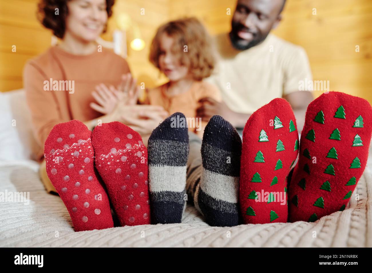 Eine Reihe von Füßen einer jungen Familie interkultureller Eltern und ihres kleinen Sohnes, die warme Wollsocken tragen und sich auf dem Doppelbett ausruhen Stockfoto
