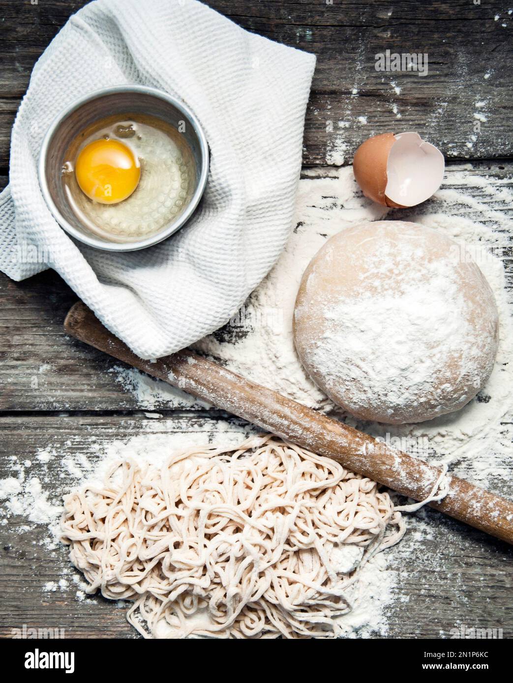 Ich mache frische Pasta. Ei, Teig, Spaghetti auf einem alten Holztisch gefüllt mit Mehl. Weißes Geschirrtuch. Stockfoto