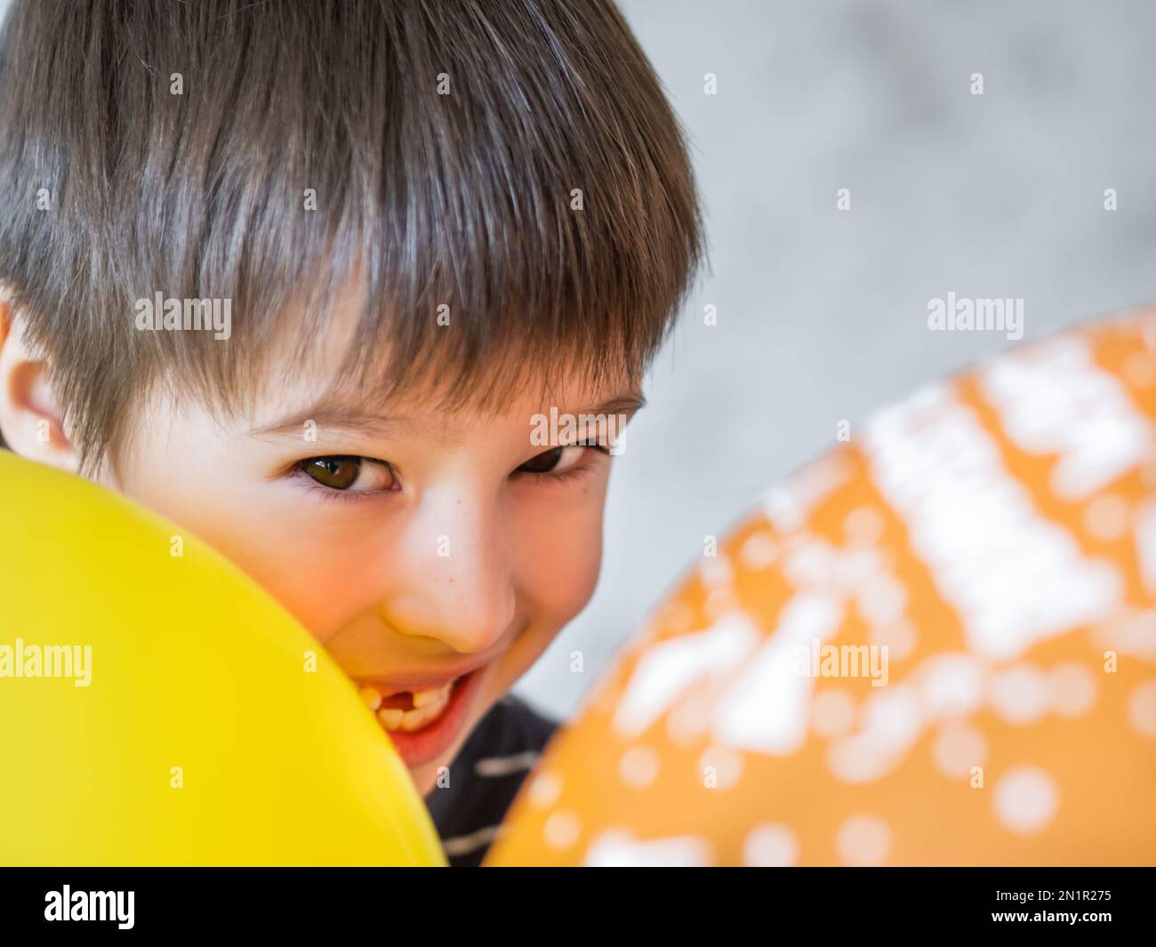 Lächelndes Kind zeigt ein Loch in einer Reihe von Zähnen in seinem Mund. Gerade ist ein Schneidezahne herausgefallen. Glückliches Kind mit Luftballons. Stockfoto