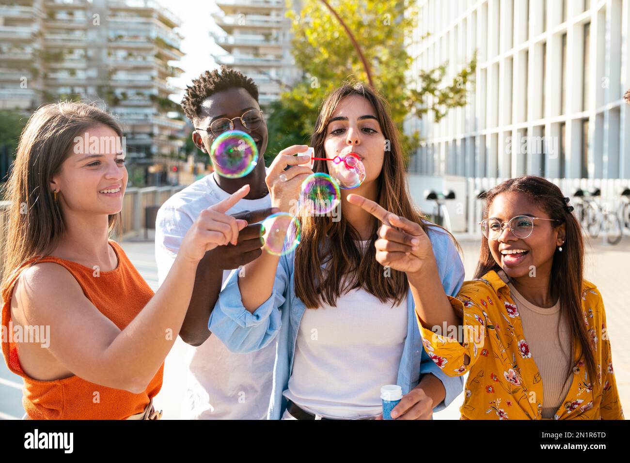 Multirassische Gruppe glücklicher Freunde, die Spaß mit Seifenblasen in der Stadt haben - fröhliche junge Freunde, die an sonnigen Tagen mit Seifenblasen lächeln - Glück Stockfoto
