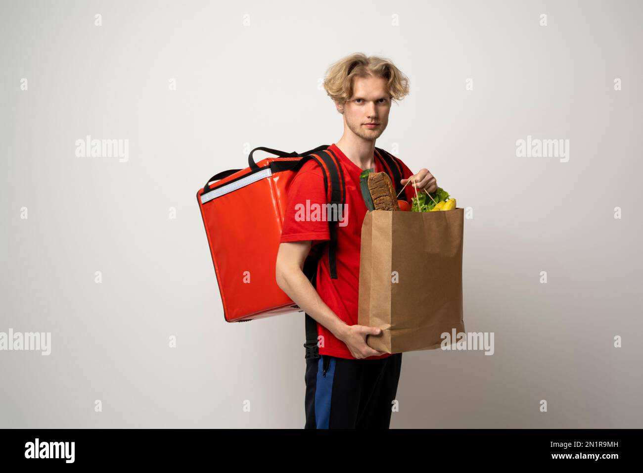 Ein attraktiver Zusteller, ein Kurier, der Lebensmittel und Getränke aus dem Laden mitbrachte, ein Supermarkt, isoliert auf weißem Studiohintergrund. Stockfoto