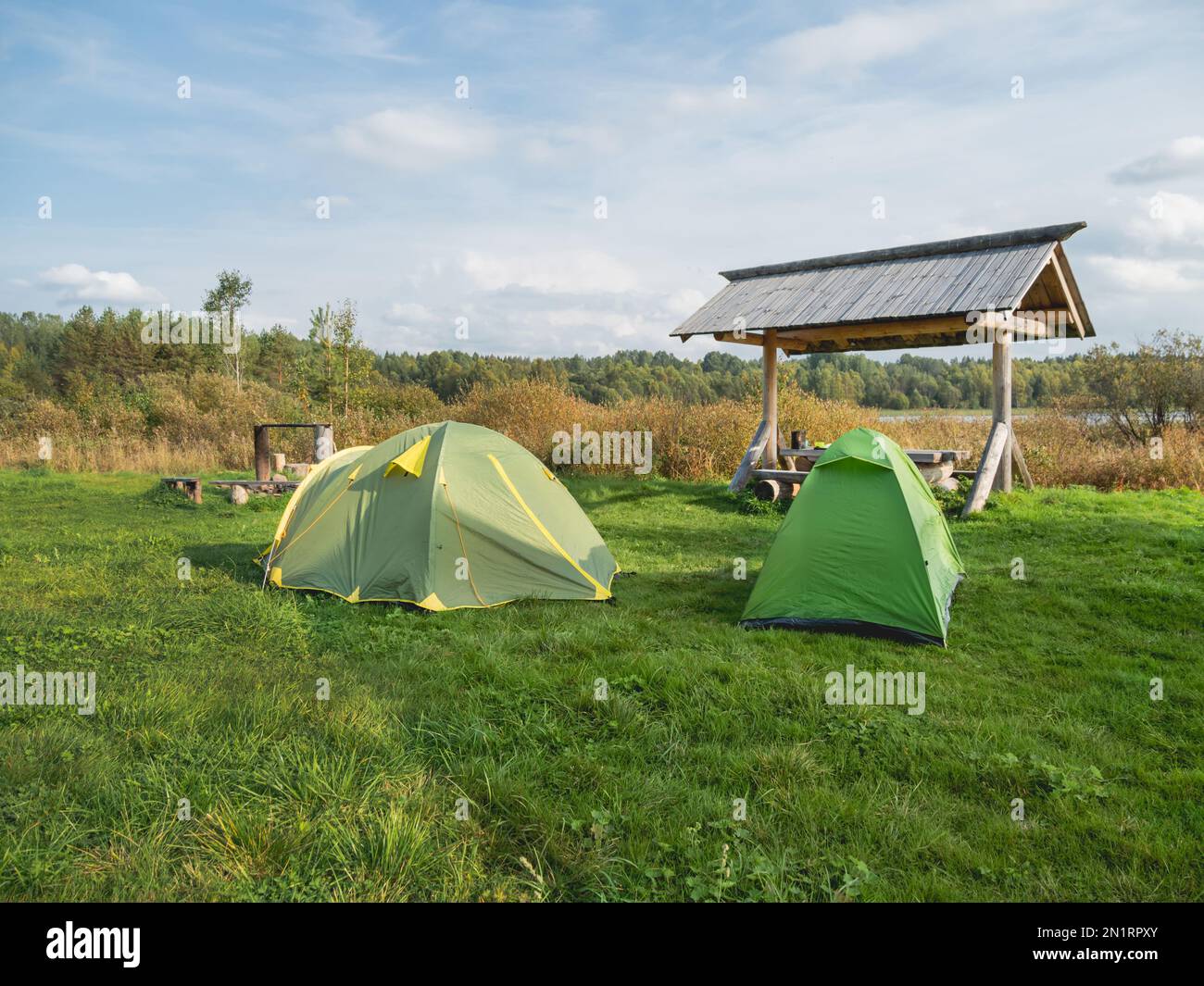 Zwei grüne Touristikzelte stehen im Camp. Holztisch, Bänke und Feuerstelle zum Campen. Wandern in Russland. Stockfoto