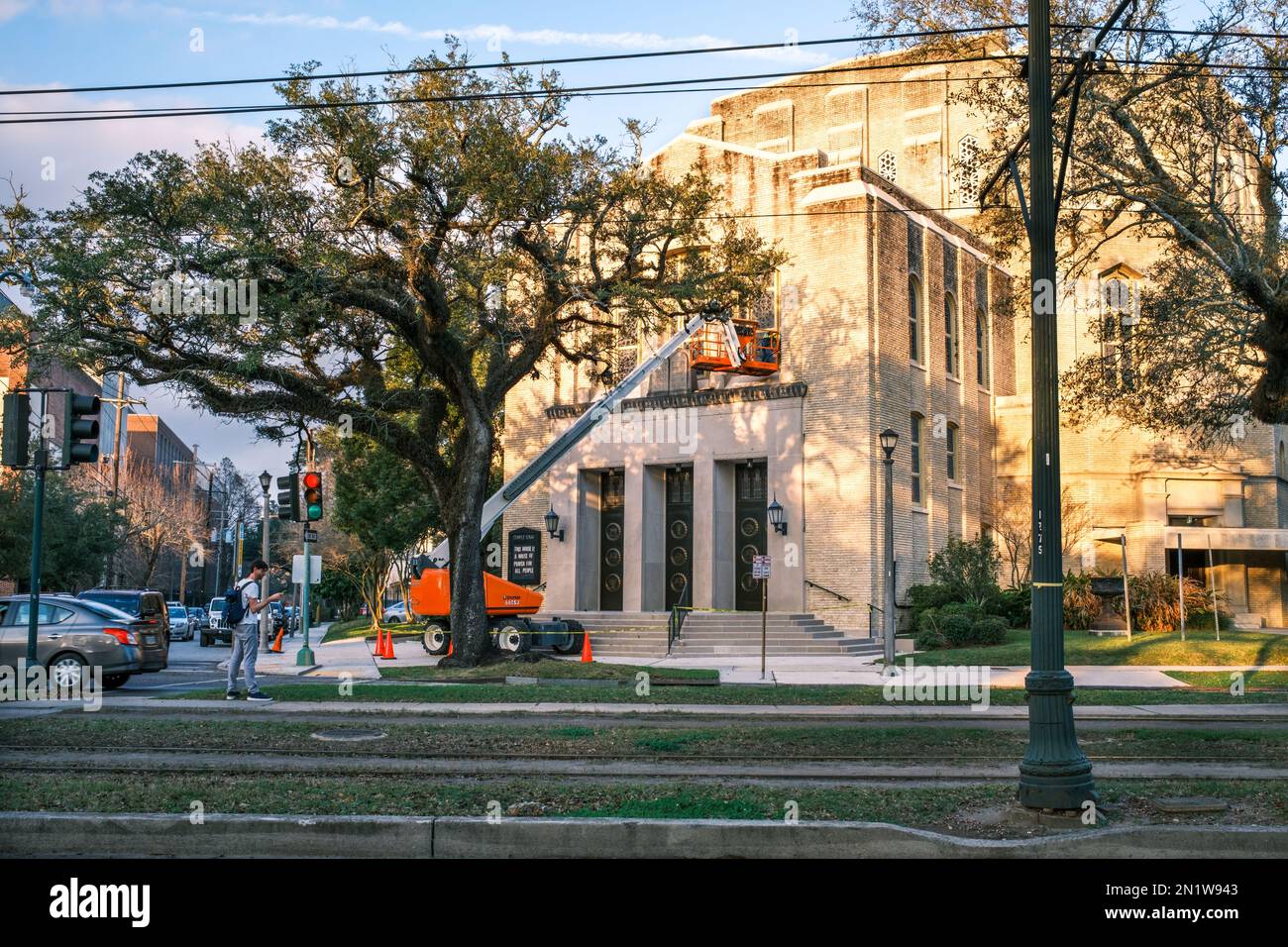 NEW ORLEANS, LA, USA - 31. JANUAR 2023: Vorderseite der Synagoge Temple Sinai, ein Reparaturarbeiter auf einem Aufzug und ein Mann, der auf einen Straßenwagen auf der St. Charles, Ich Bin'S Stockfoto