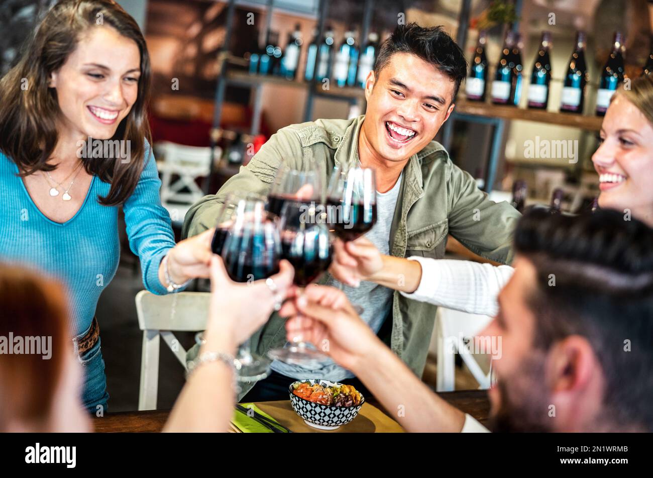 Trendige multikulturelle Freunde, die Rotwein im Sushi Poke Bowl Restaurant anstoßen - Lifestyle-Konzept für Speisen und Getränke mit fröhlichen Menschen, die Spaß haben Stockfoto
